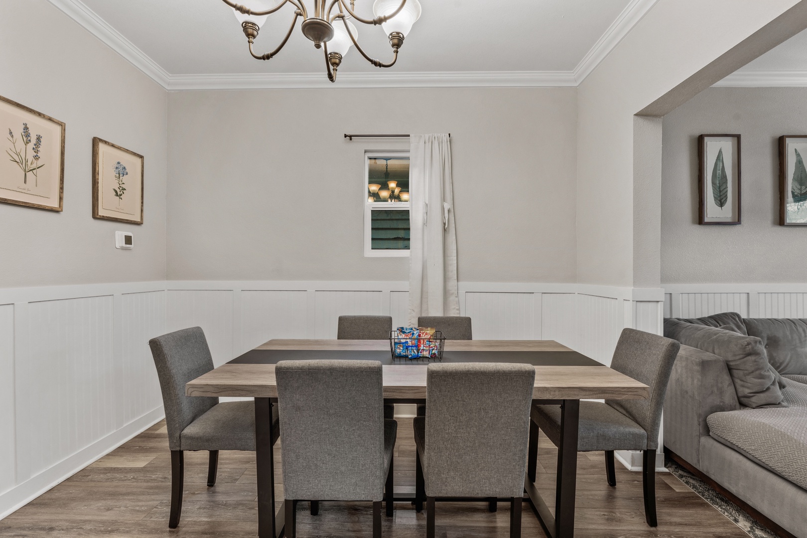 Your dining space features a sophisticated table for six with comfortable upholstered chairs, elegant chandelier lighting, and charming botanical artwork to set the mood for memorable meals.