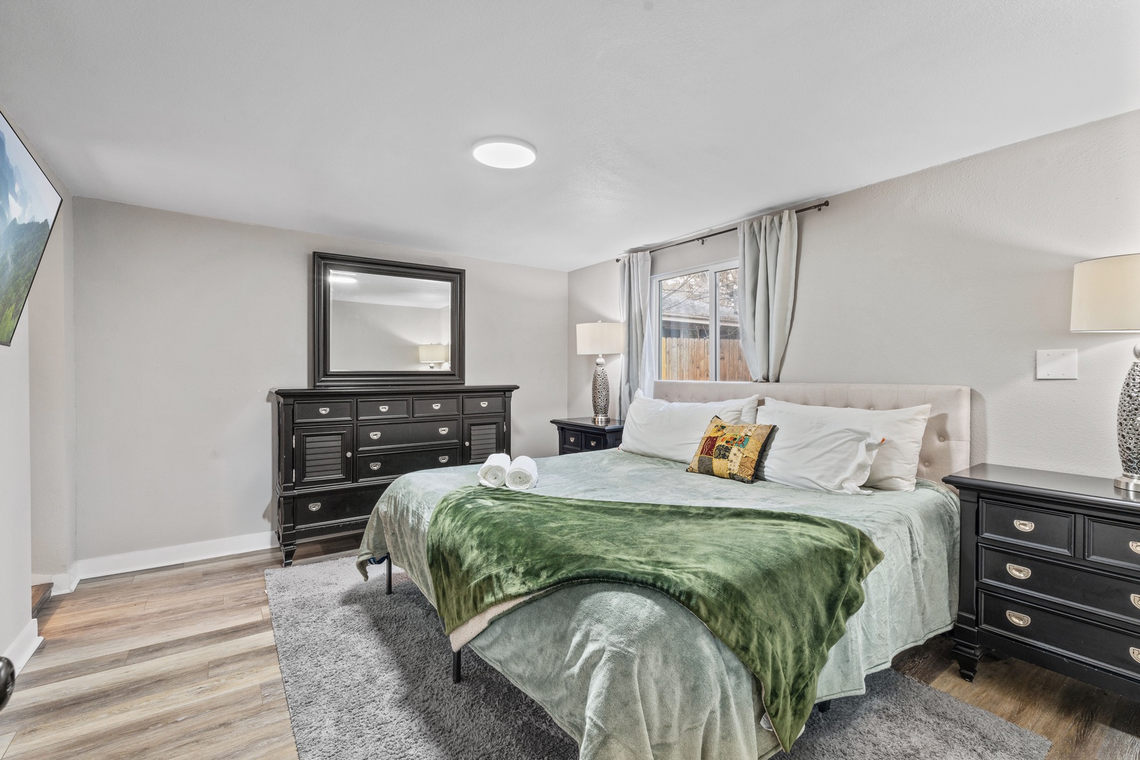 Rest comfortably in your stylish bedroom featuring a plush king bed, elegant dark wood furniture, and soft natural lighting from the window.