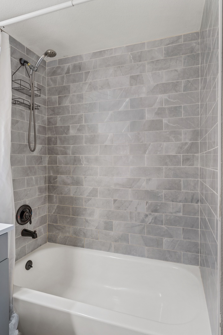 Refresh after your adventures in this modern tub-shower combo featuring elegant gray marble-look tile and convenient shower caddy storage.