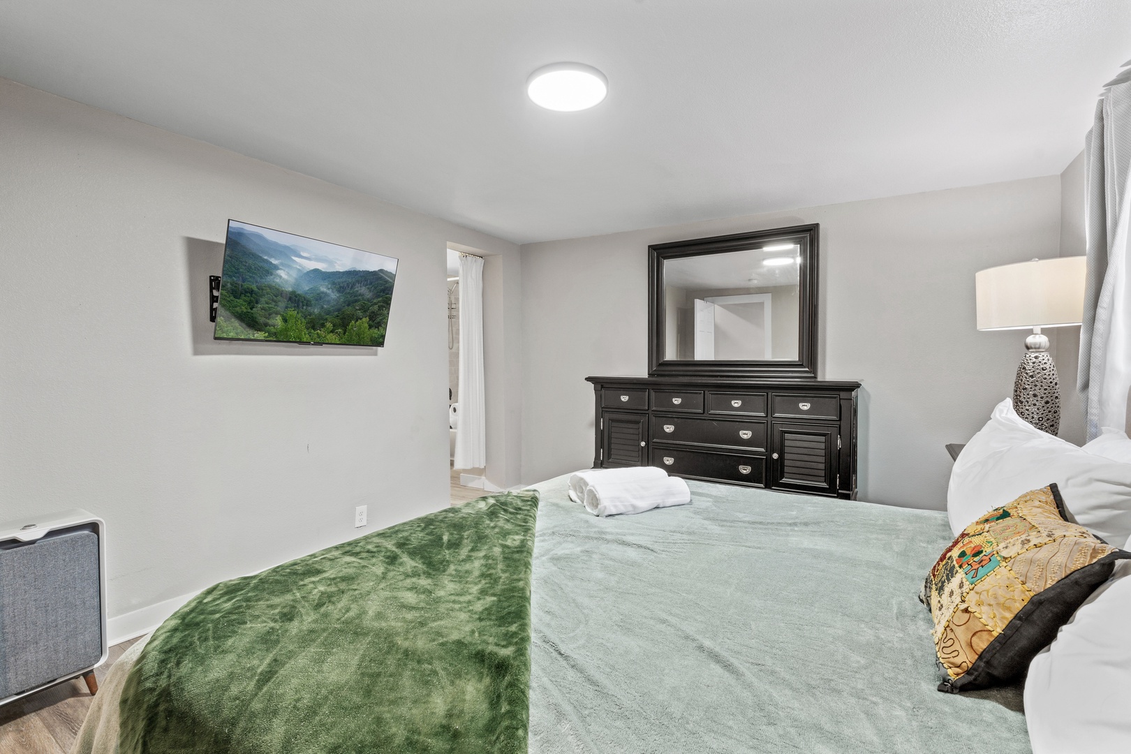 Relax in your peaceful bedroom featuring a comfortable bed with soft linens, elegant dark wood furnishings, and modern amenities including a flat-screen TV.