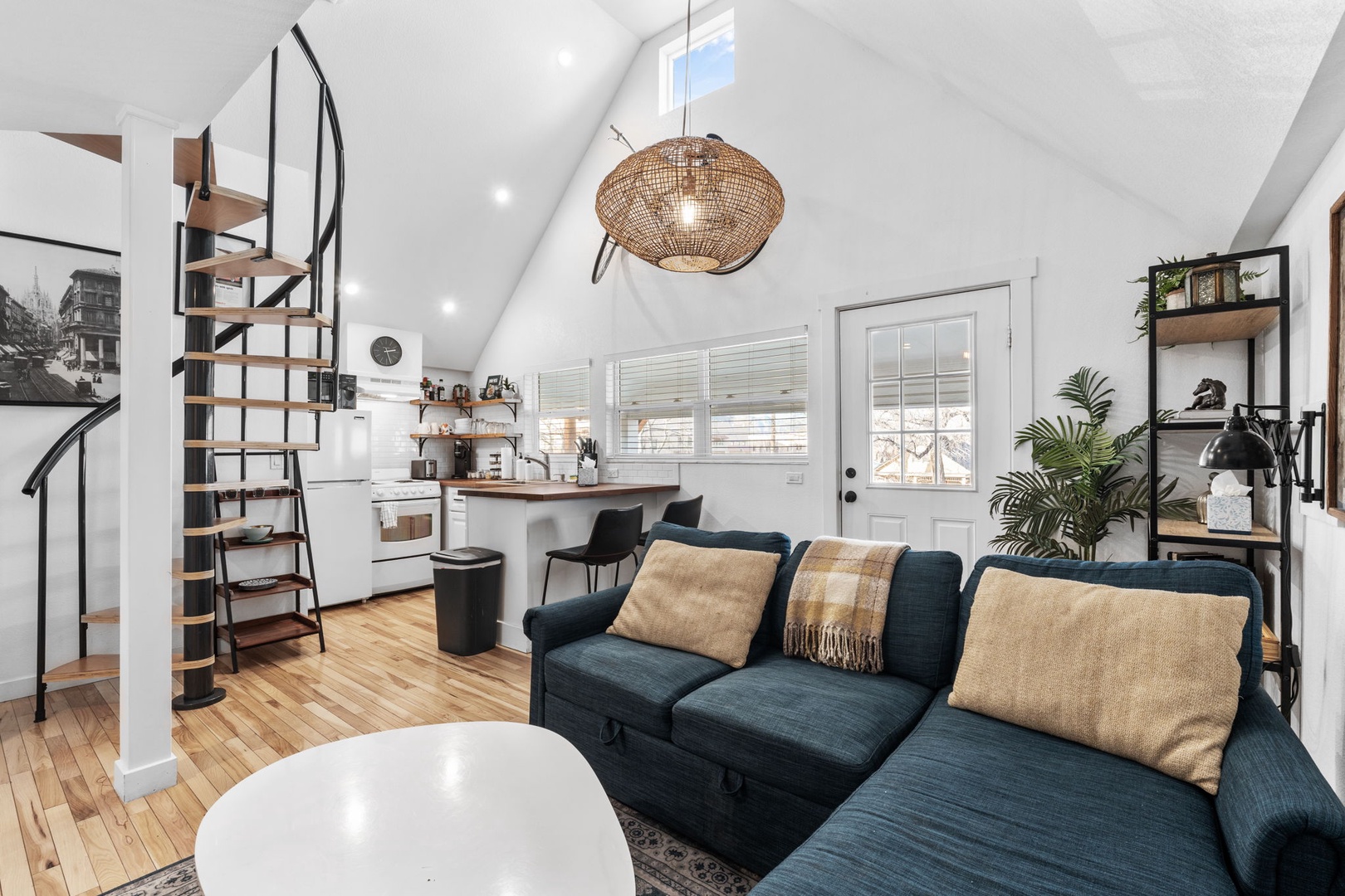 Relax in your stylish open-plan retreat with cozy blue sectional, modern kitchen, and charming spiral staircase leading to your private loft.