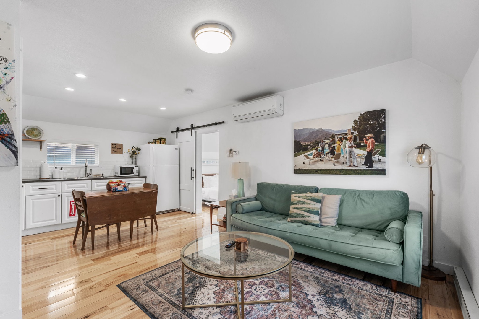 Relax in your bright, modern space with a stylish teal sofa, gleaming hardwood floors, and fully equipped kitchen perfect for preparing meals during your stay.