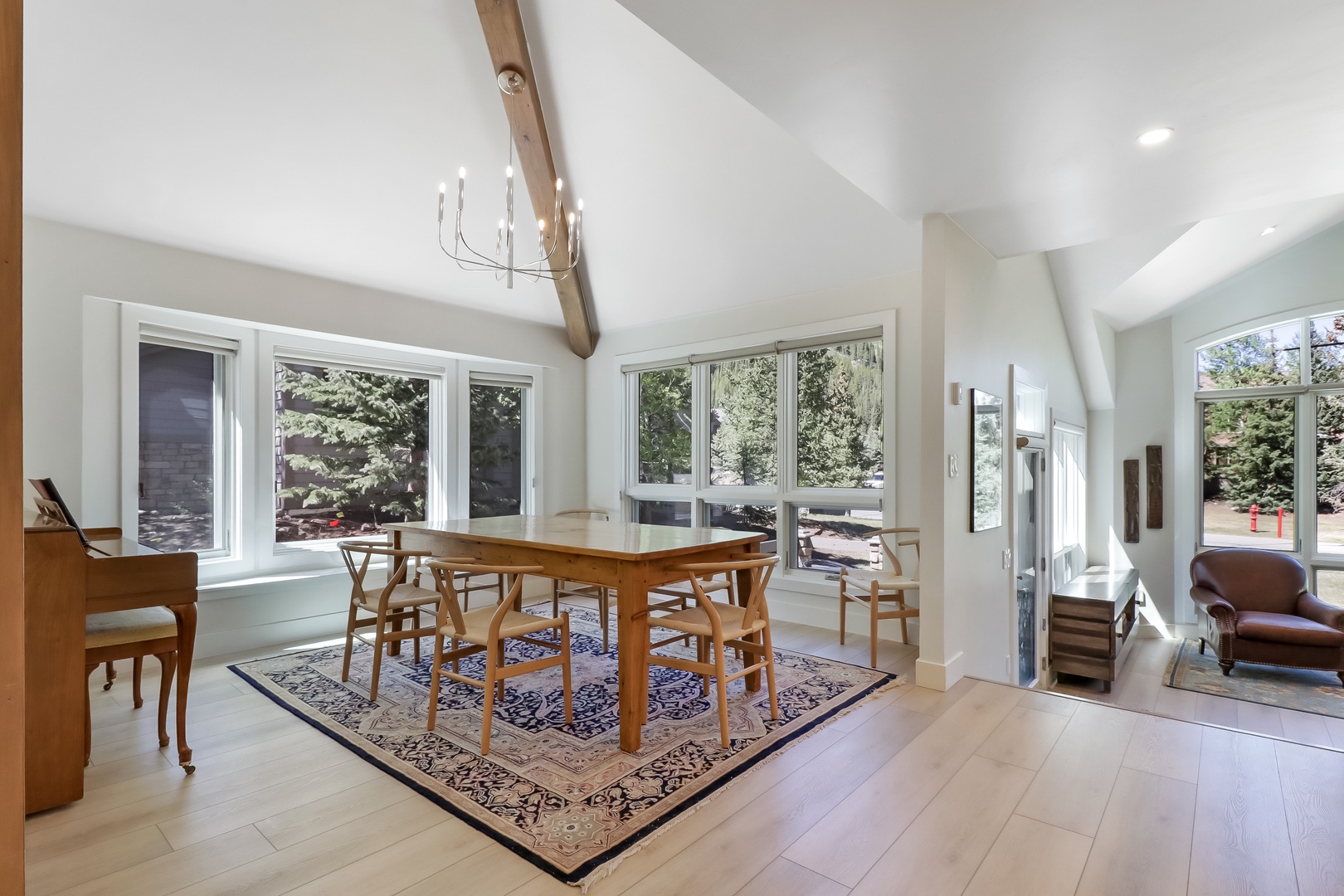 Gather around the handcrafted dining table beneath soaring vaulted ceilings and rustic wooden beams. Sunlight pours through expansive windows, framing peaceful treetop views while you share meals in this warm, airy space.