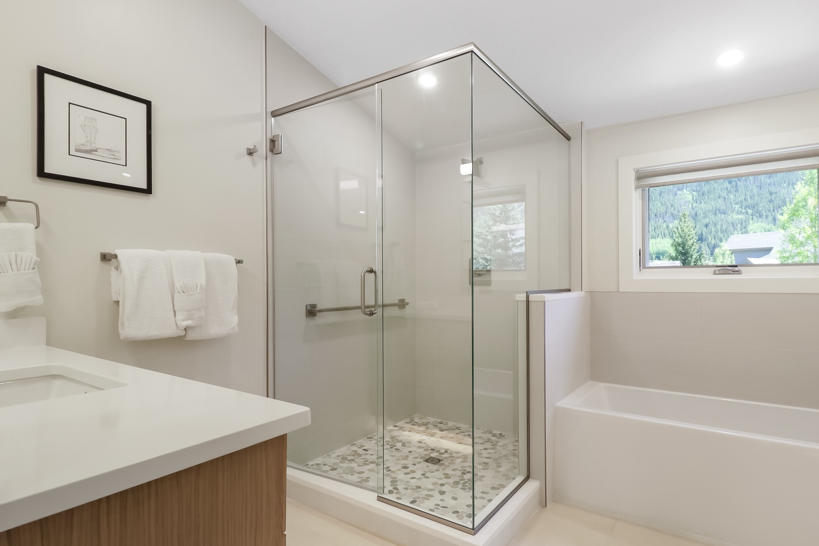Step into your spa-inspired bathroom where a sleek glass shower and a deep soaking tub await after a day exploring the mountains you can glimpse through the window.