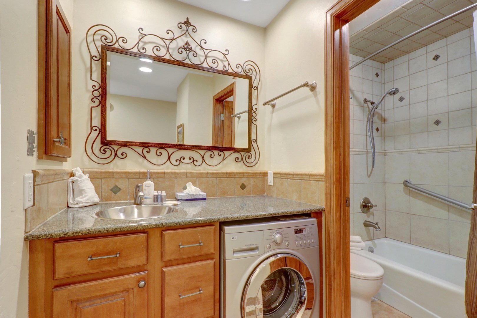 Convenient bathroom featuring a tiled tub/shower combination and an in-unit washer/dryer with granite countertop. Perfect for extended stays and family convenience.