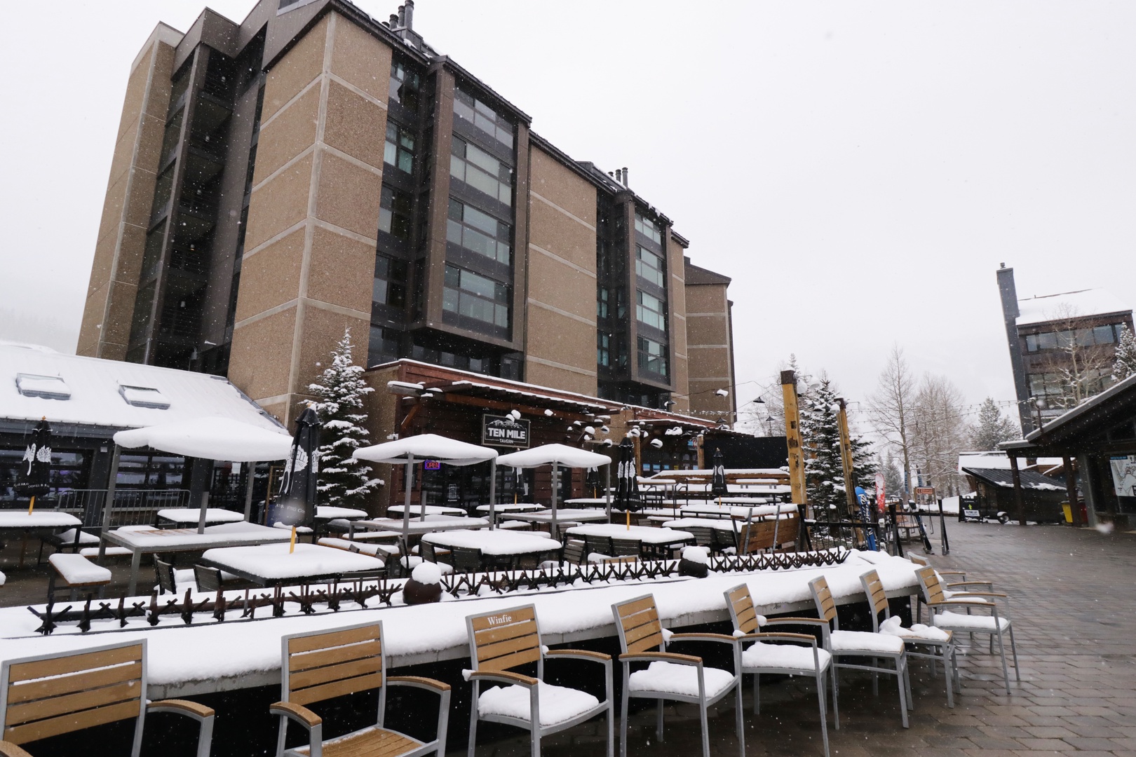A winter scene with fresh snow blanketing outdoor seating and mountain views, capturing the alpine charm of the surrounding resort village.