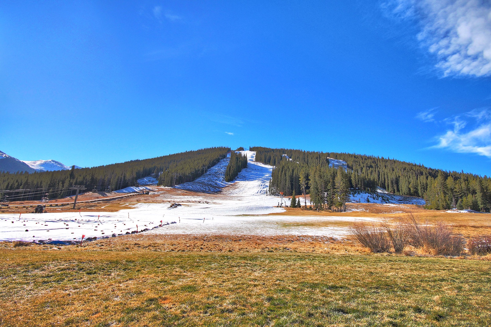 Mountain ski slopes with snow-covered runs cutting through forested hills under bright blue skies.