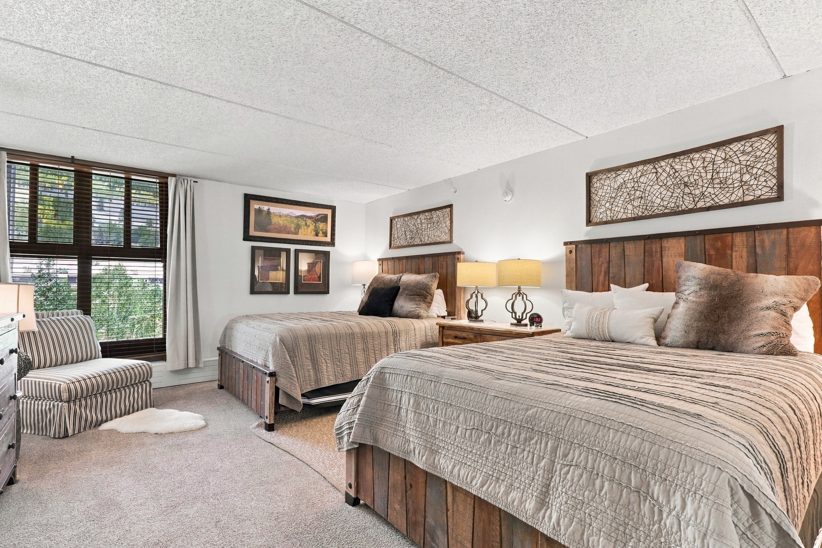 Unwind in your cozy bedroom featuring two inviting beds dressed in neutral tones, rustic wood furnishings, and a plush armchair by the window—your peaceful mountain retreat awaits.
