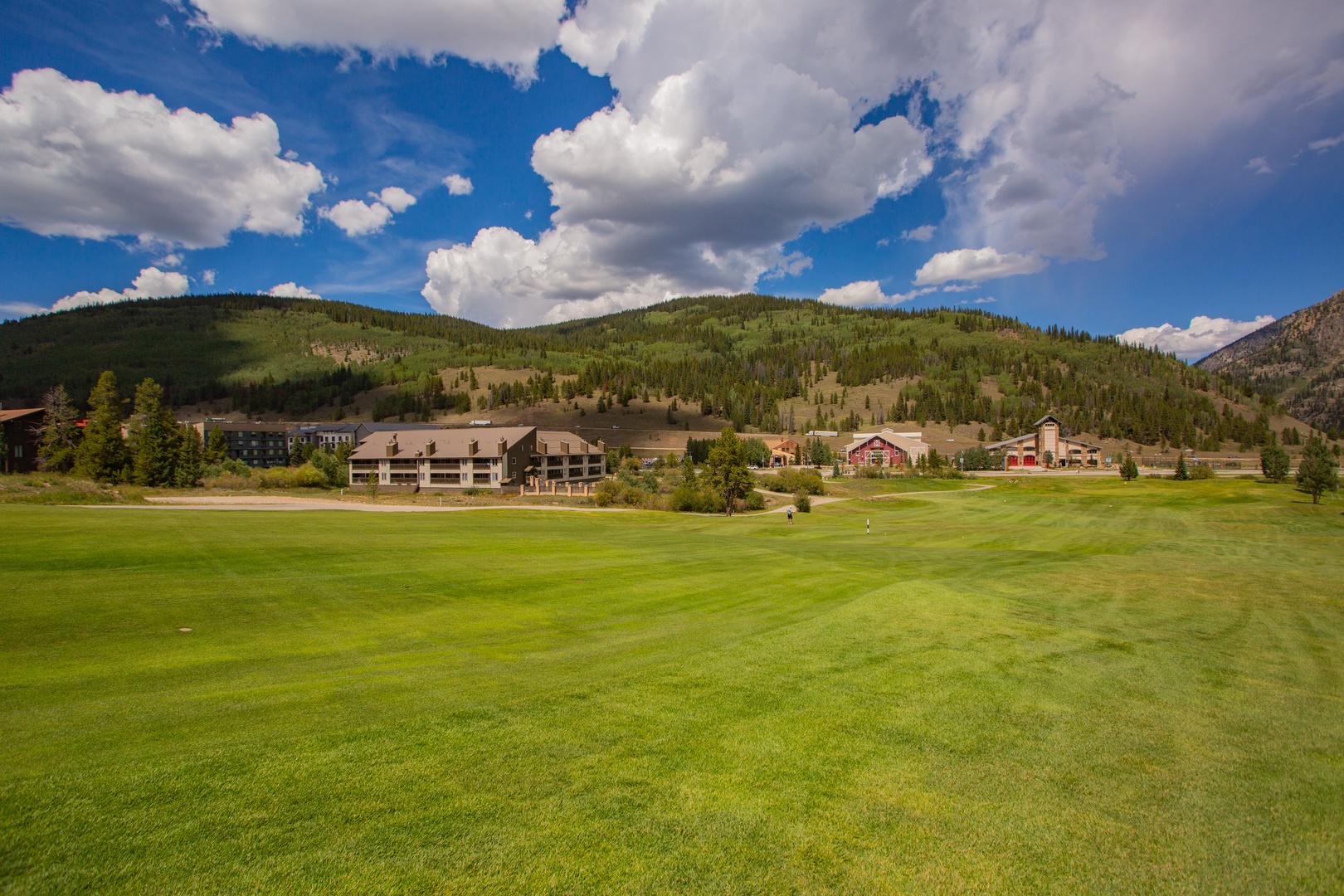 A serene mountain valley property featuring an 18-hole championship golf course surrounded by forested hillsides and dramatic summer skies. The lodge and neighboring buildings provide easy access to the expansive fairways and natural landscape.