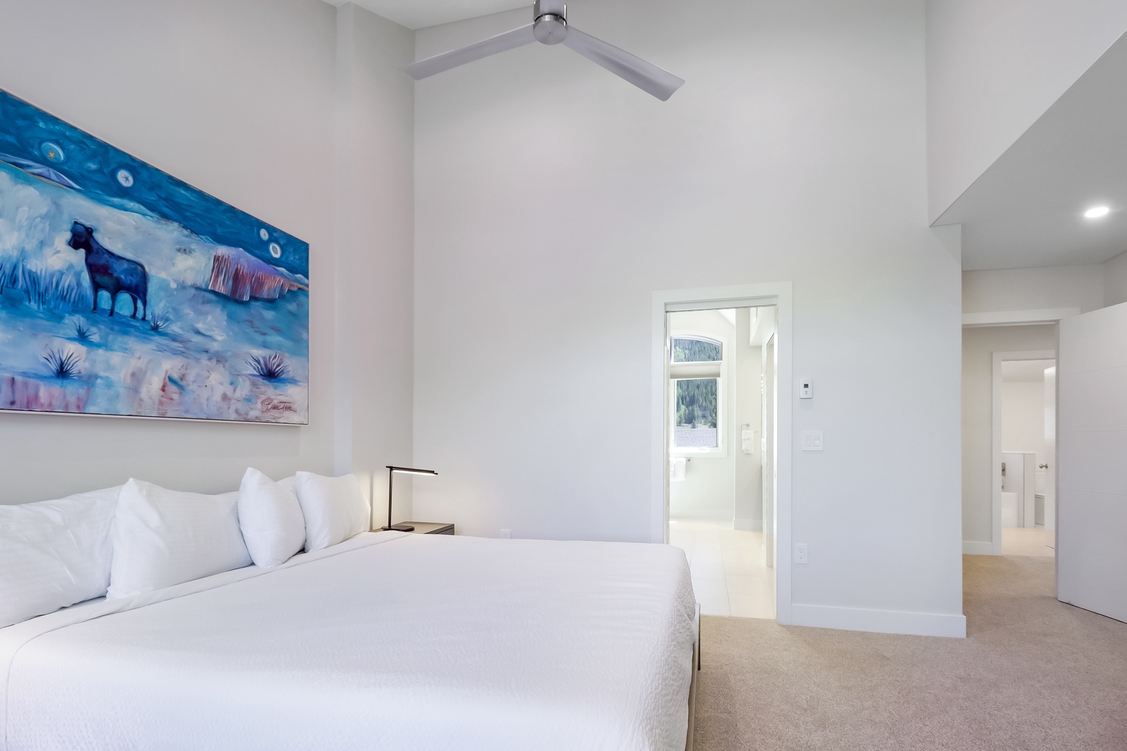 Unwind in your bright, modern bedroom with crisp linens, a calming ceiling fan, and unique artwork to set a peaceful tone.