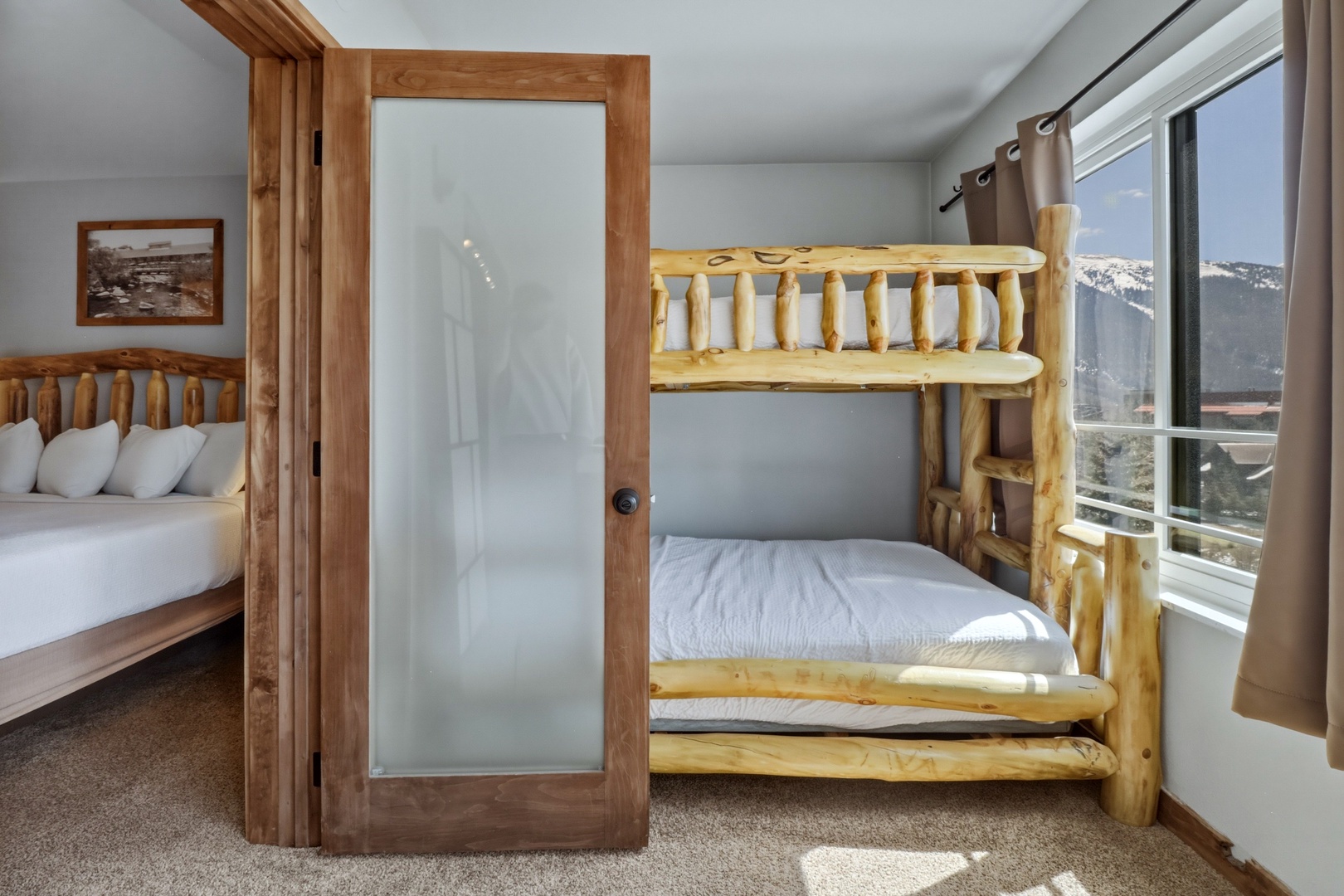 Your cozy bedroom features handcrafted log bunk beds and stunning mountain views through large windows, creating the perfect alpine retreat.