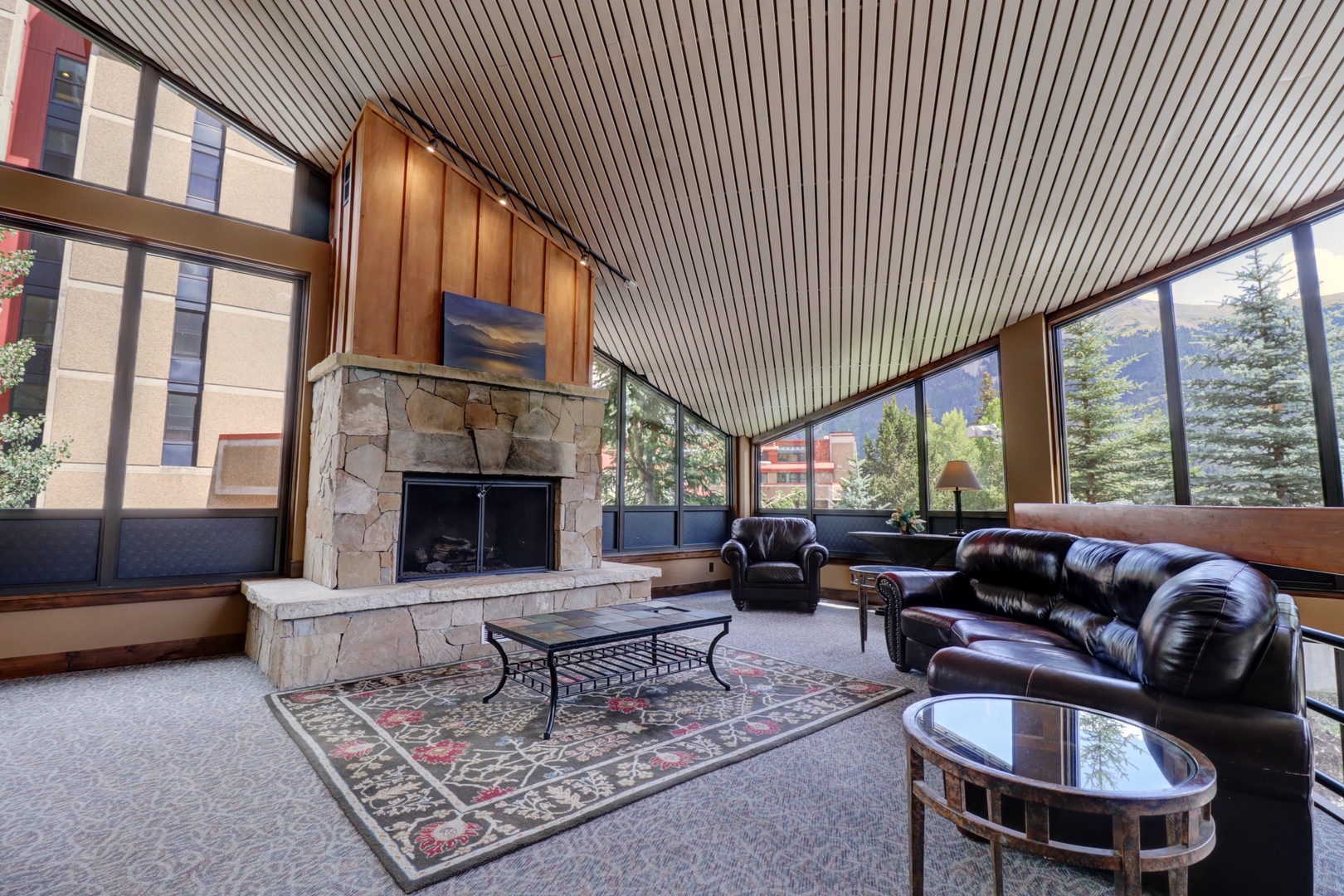 Relax in this stunning great room with soaring ceilings, a beautiful stone fireplace, and expansive windows framing natural light and surrounding greenery—your perfect mountain retreat.