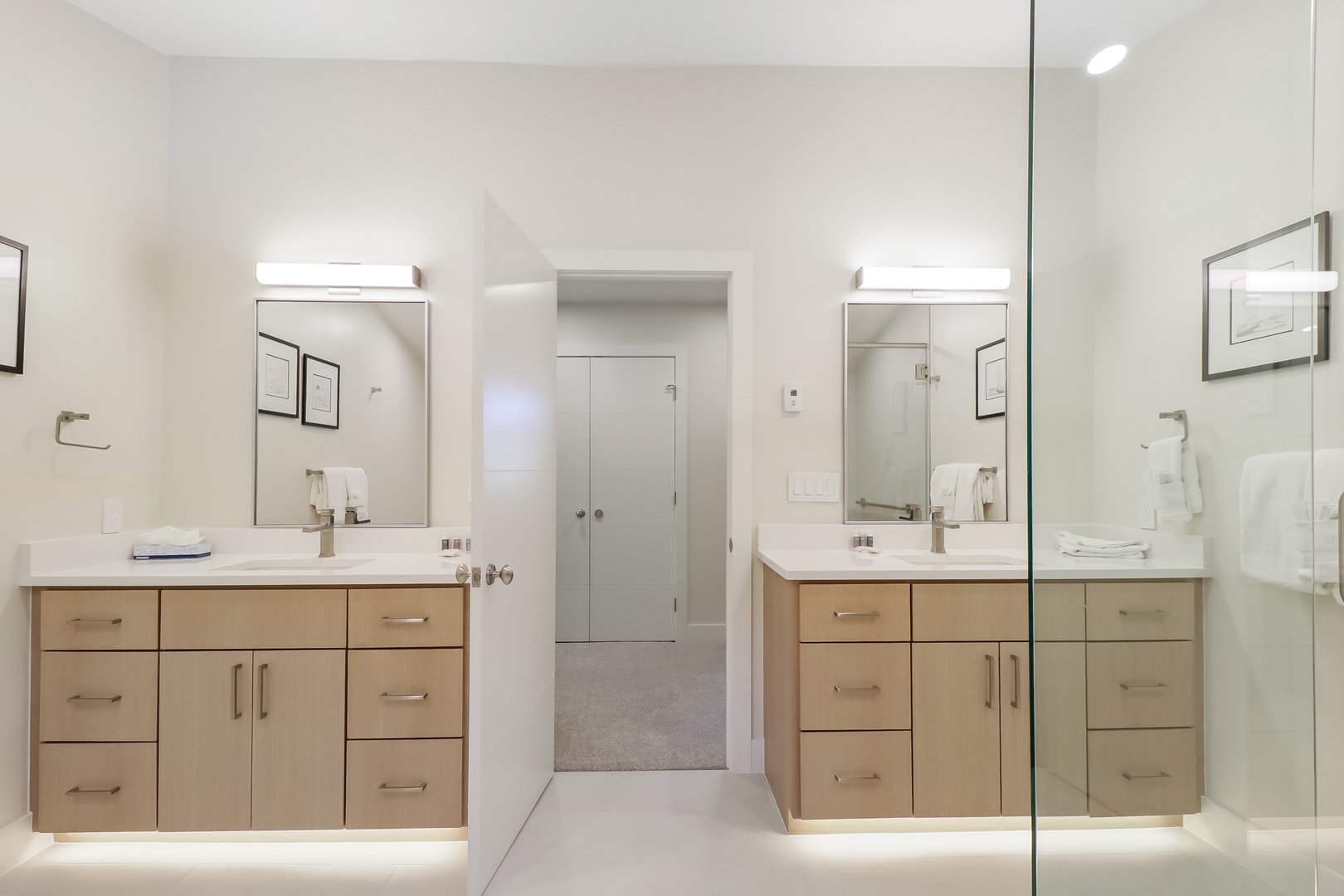 Your spacious dual-vanity bathroom offers sleek modern design with warm wood cabinetry and abundant counter space. Bright ambient lighting and a frameless glass shower create a spa-like retreat for your morning and evening routines.