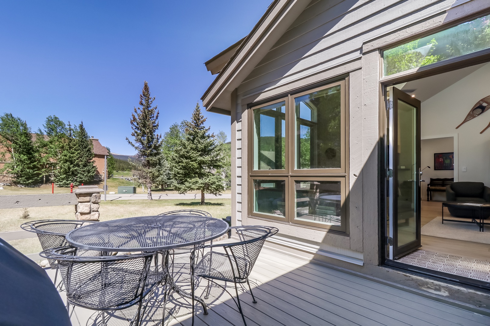 The property is nestled in a tranquil mountain setting surrounded by evergreens, with a spacious deck offering views of the peaceful neighborhood and natural landscape beyond.