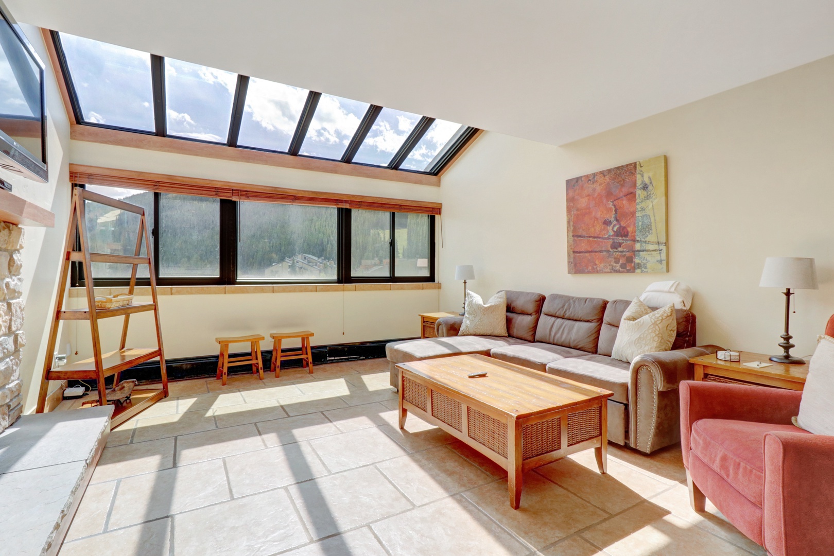Spacious living room flooded with natural light from a large skylight and wide windows that frame breathtaking mountain scenery. Comfortable furnishings create a perfect après-ski gathering space.