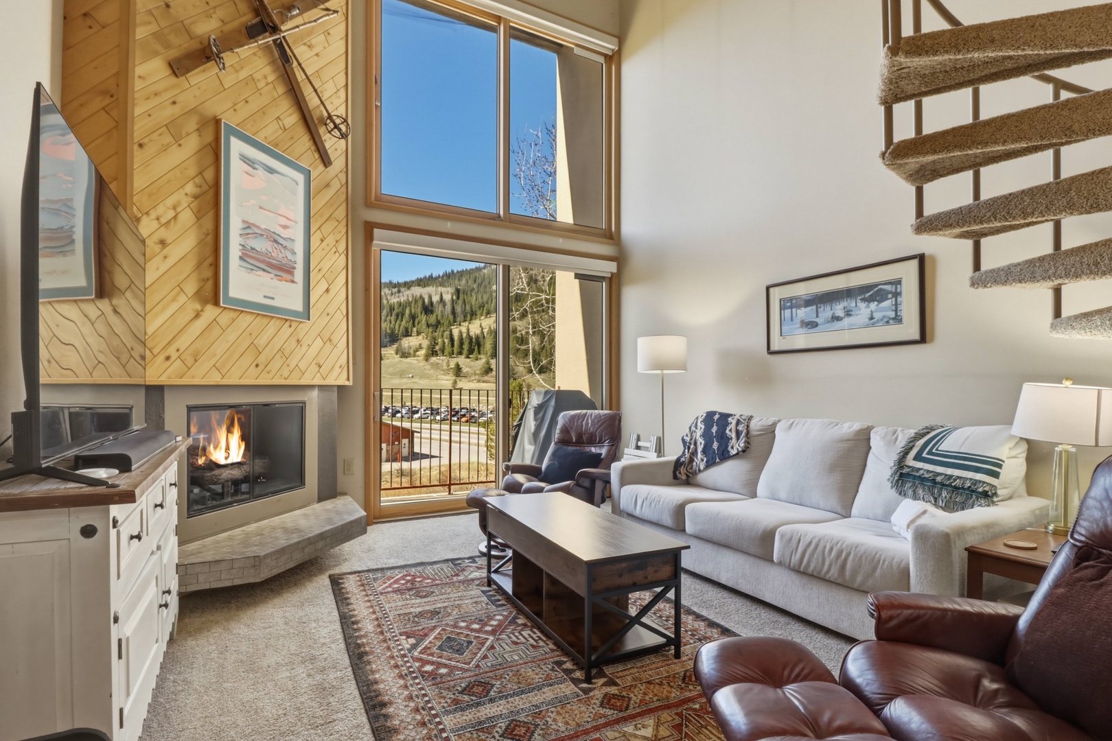 Cozy up in your inviting living room with crackling fireplace, plush seating, and stunning mountain views through soaring windows.