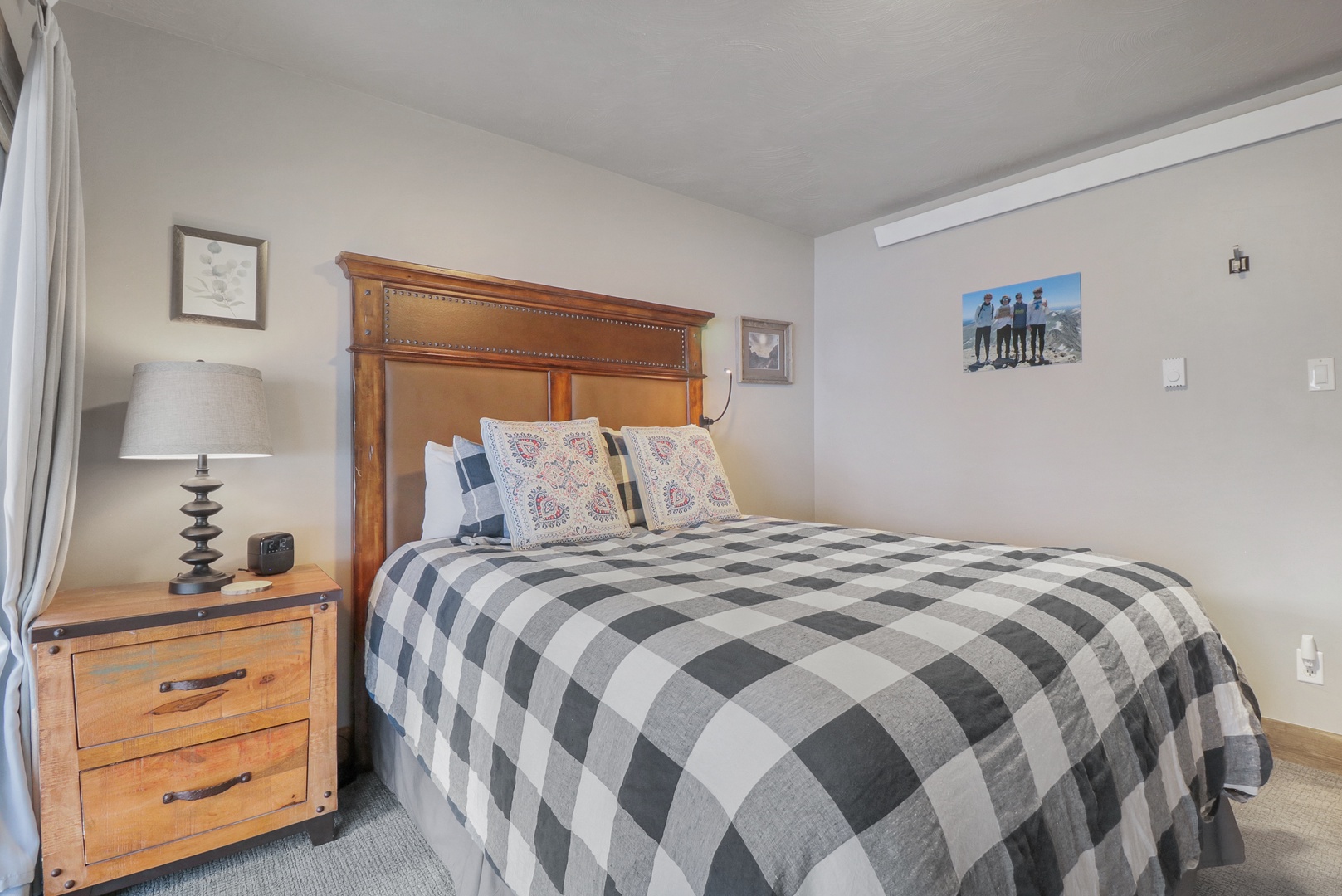 Sink into the warmth of this thoughtfully designed bedroom where rustic charm meets modern comfort. The rich wooden headboard and cozy plaid bedding create your perfect mountain retreat sanctuary.