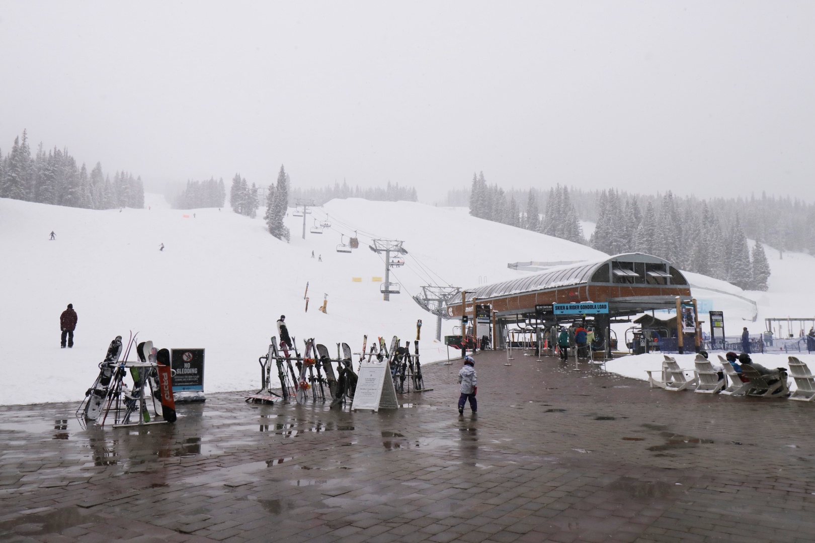 A ski resort base area surrounded by snowy slopes and evergreen trees, offering access to winter mountain activities and chairlift facilities.