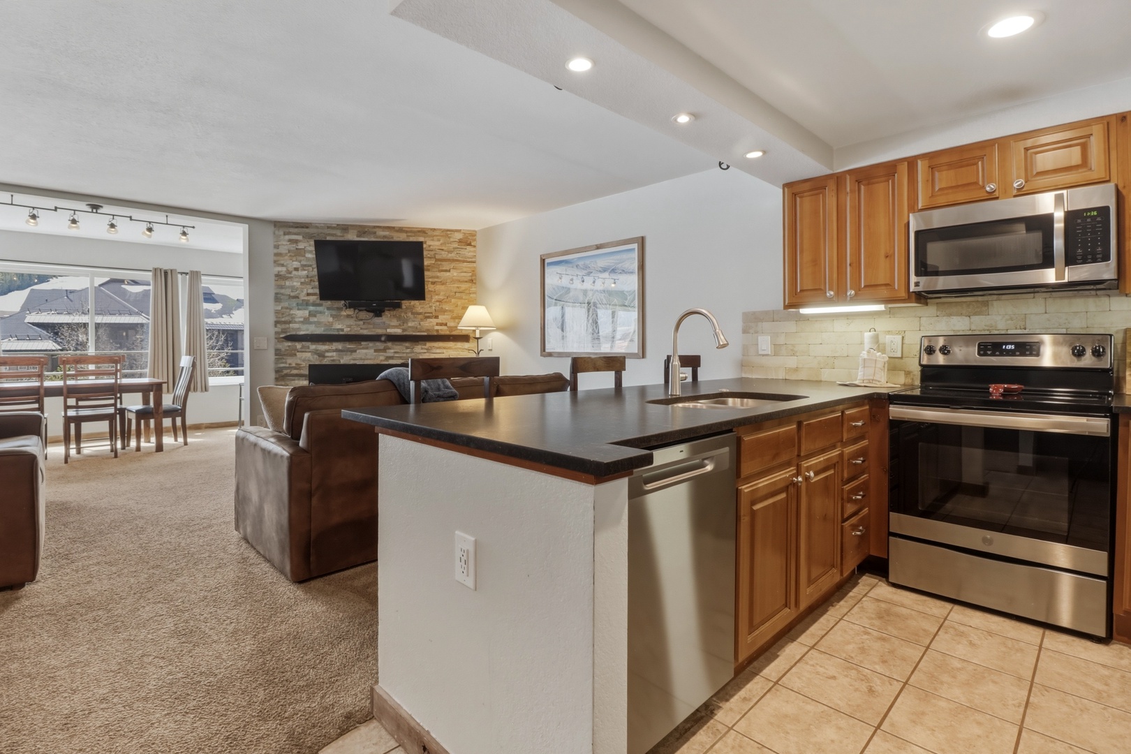 Your open-concept kitchen flows seamlessly into the cozy living area, perfect for preparing meals while chatting with loved ones by the stone fireplace.