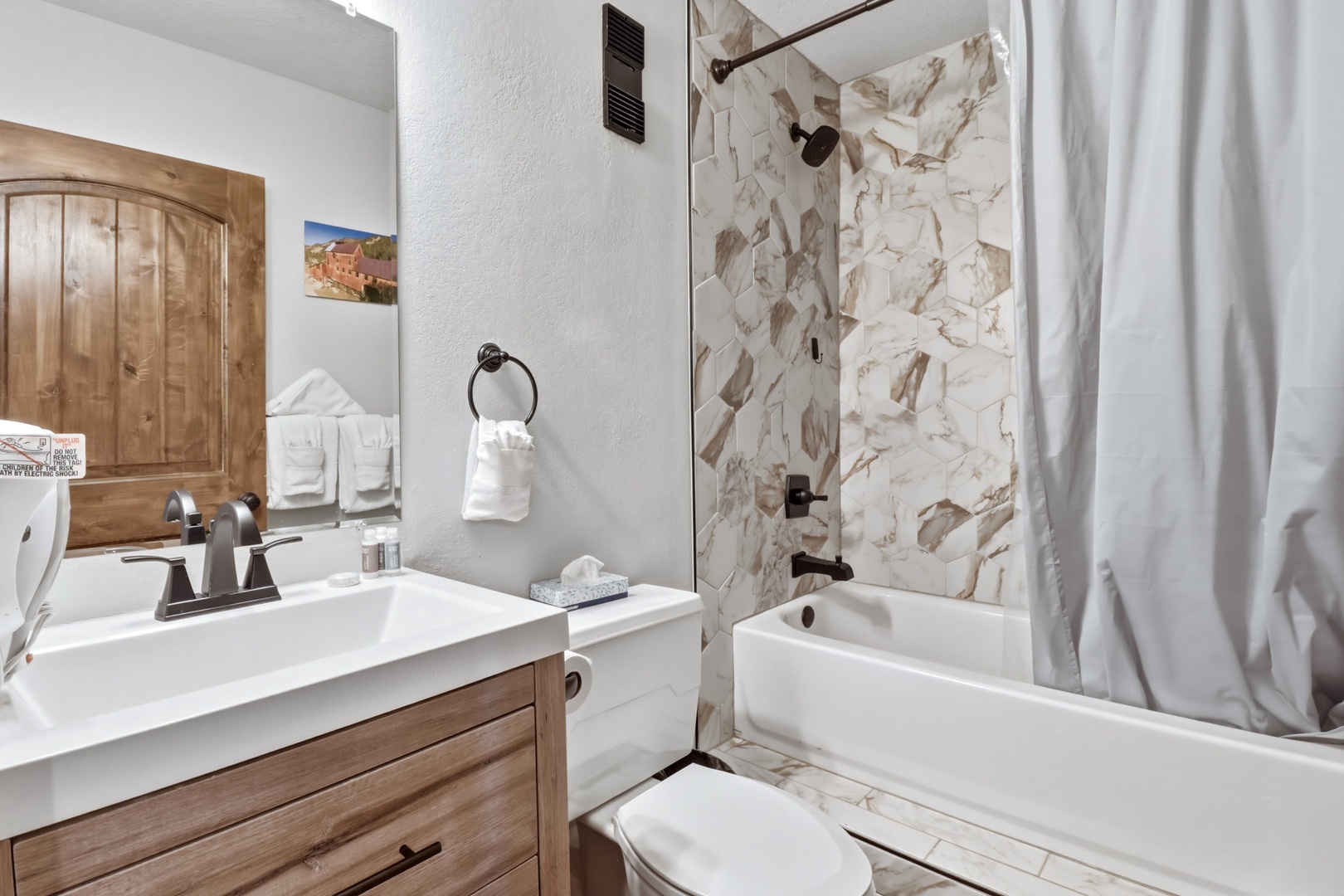 Refresh in your stylish bathroom featuring elegant marble-inspired tile, warm wood vanity, and pristine tub-shower combo for relaxing soaks.