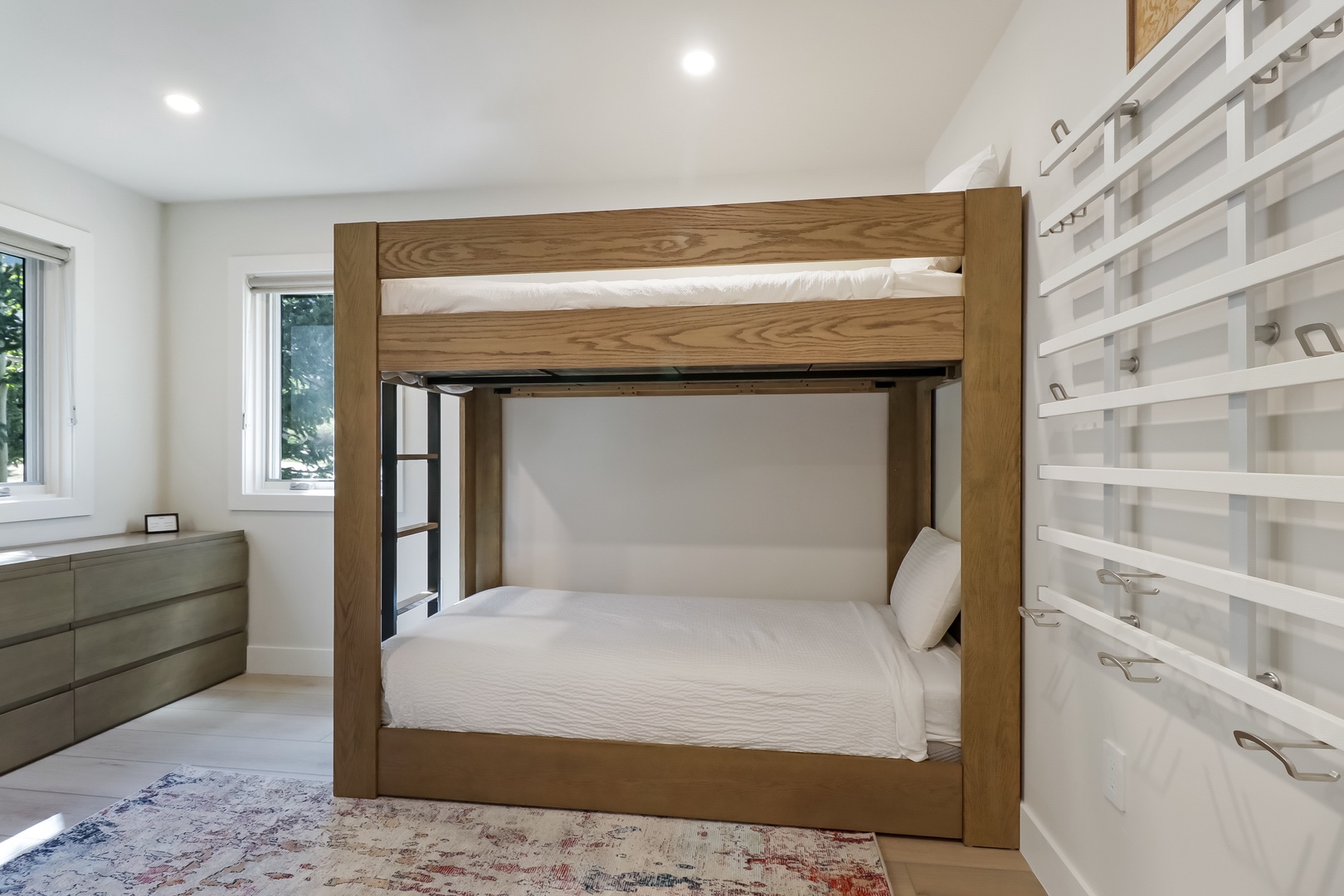 Your bright, cozy bedroom features a sturdy wooden bunk bed with crisp white linens, plenty of natural light, and ample storage drawers to keep your belongings organized.