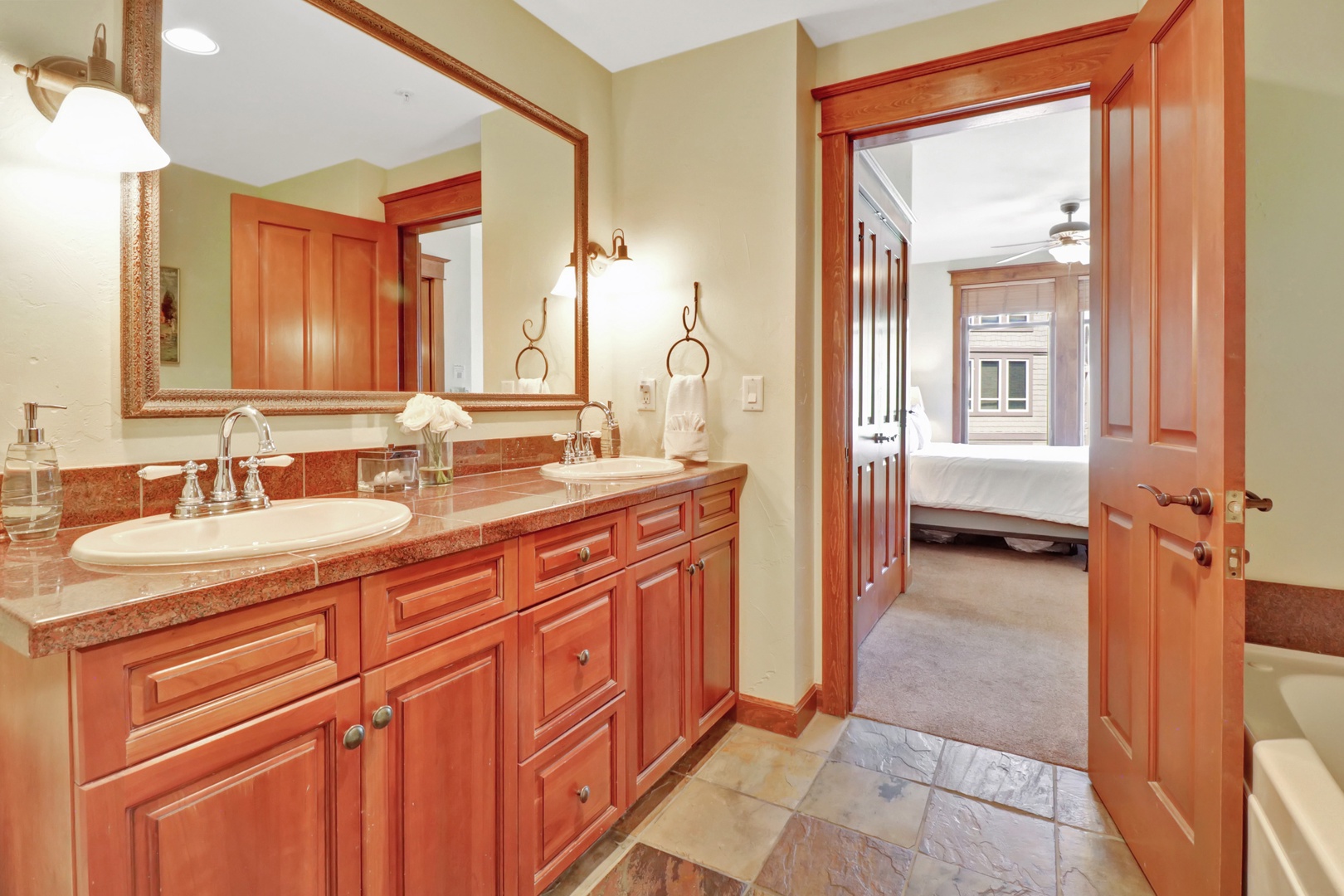 Freshen up in your spacious bathroom with warm wood cabinetry, granite counters, and a large mirror. The open doorway invites you into your cozy bedroom just beyond.