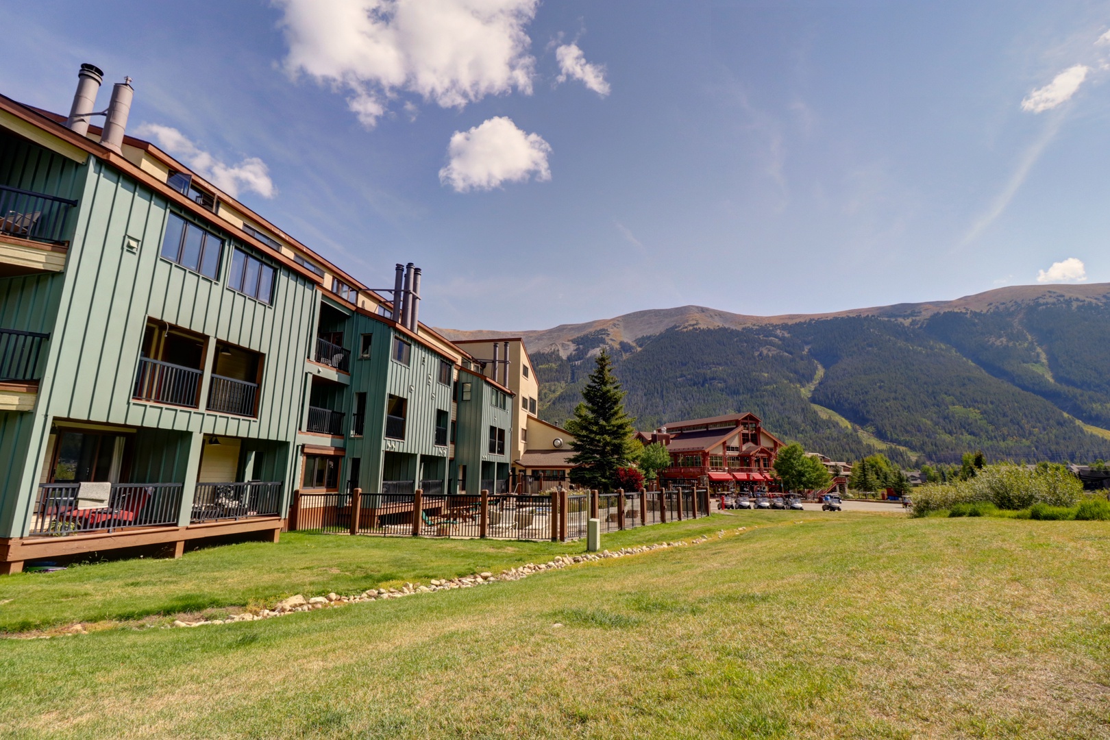 Multi-story vacation rental buildings with mountain backdrop and manicured lawn area.