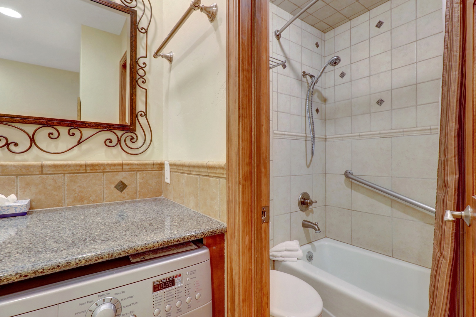 Convenient bathroom featuring a tiled tub/shower combination and an in-unit washer/dryer with granite countertop. Perfect for extended stays and family convenience.