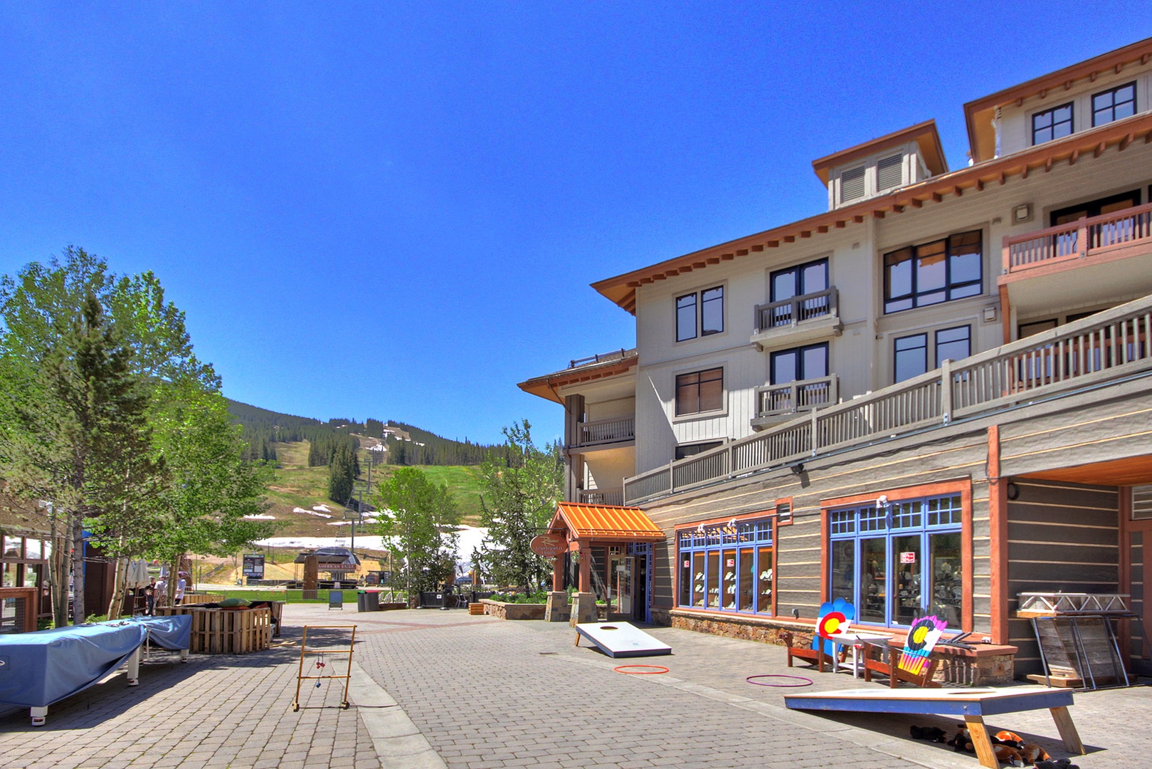 The property is situated in a mountain resort area with ski slopes visible in the background and shops at ground level.