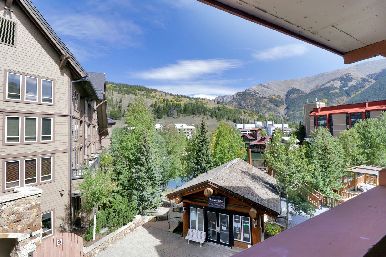 A scenic mountain village with forested slopes and alpine peaks visible beyond the surrounding buildings and trees.