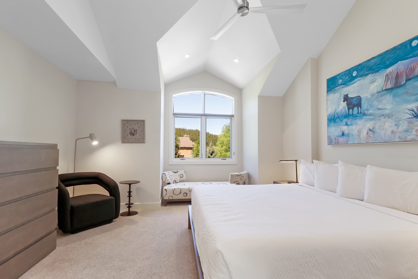 Relax in your bright, airy bedroom with soaring vaulted ceilings, a plush bed, and peaceful natural views. A cozy reading chair and stylish art create the perfect retreat.