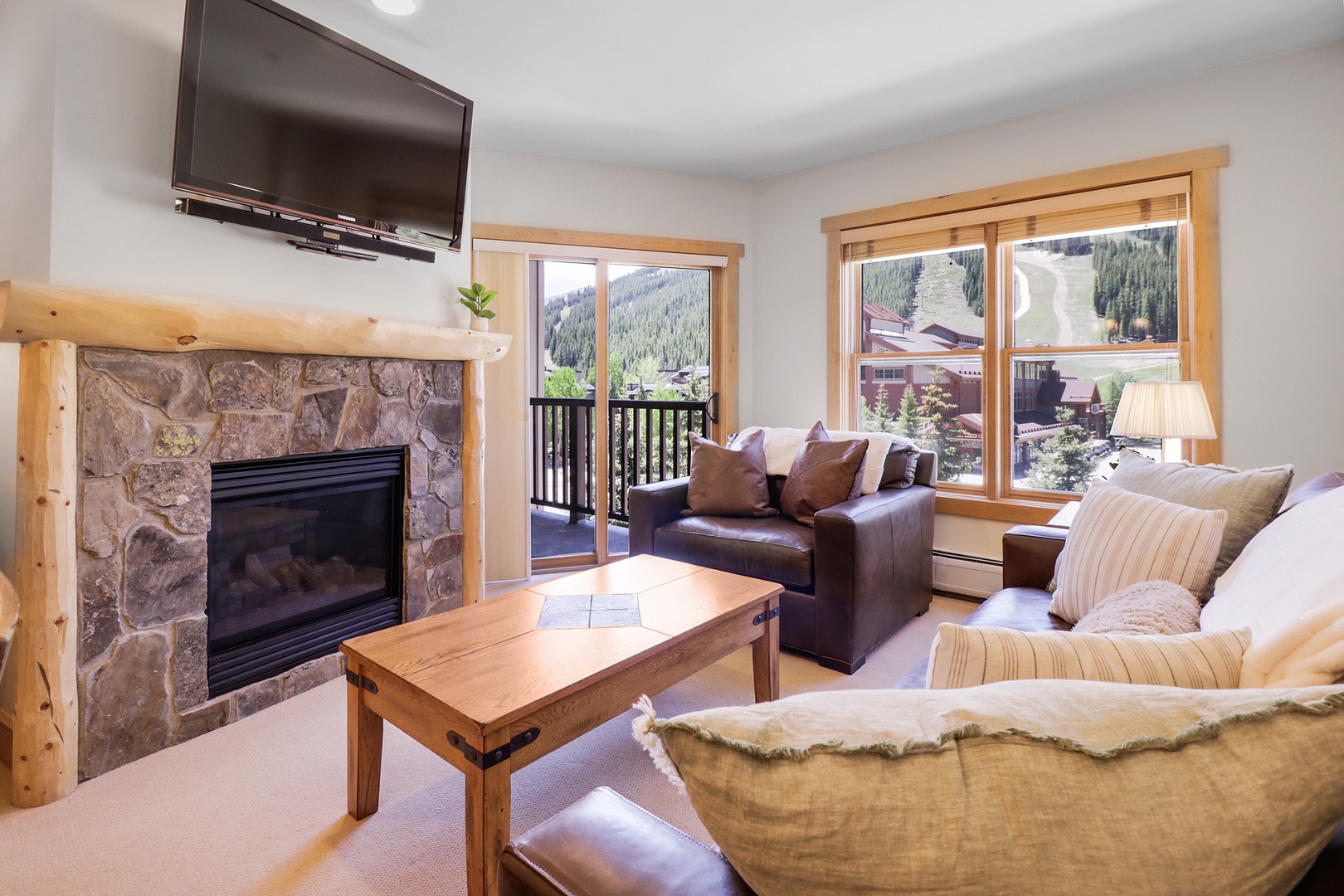 Relax in your cozy living area with a stone fireplace, mountain views, and plush seating after a day on the slopes.