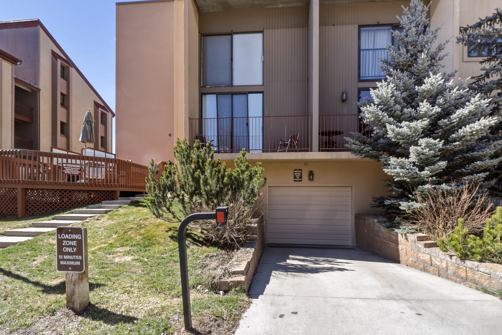 Modern townhome with private garage and balcony, nestled among mature evergreens in a peaceful residential setting.