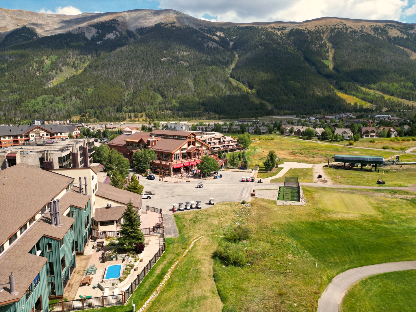 Aerial view of mountain resort town with ski slopes, residential buildings, and dramatic alpine peaks forming the scenic backdrop.