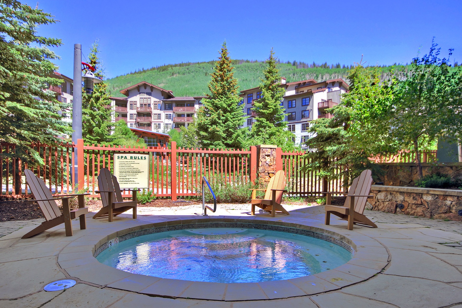 An inviting outdoor hot tub nestled among Adirondack chairs, with mountain views and verdant greenery setting the scene for relaxation at the resort.