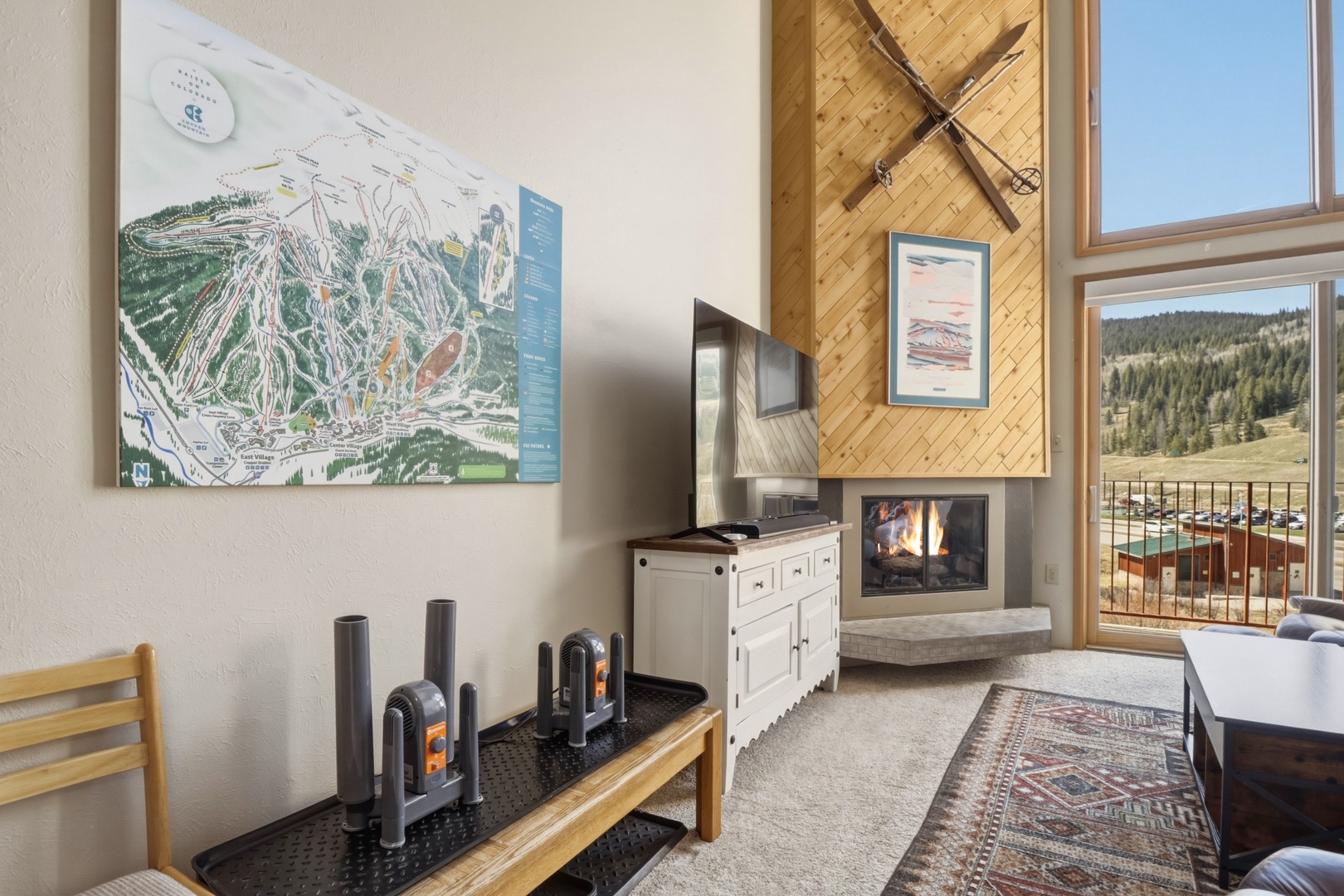 Your cozy mountain retreat features a crackling fireplace and stunning views of forested hills through floor-to-ceiling windows.