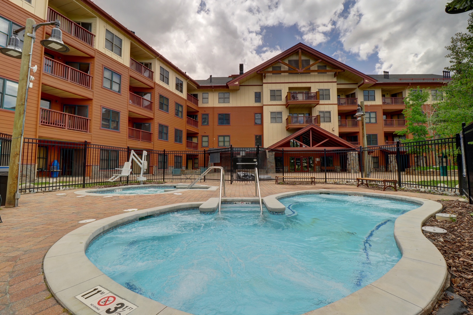 Mountain-style resort property with multi-story lodging wings framing an outdoor pool courtyard area, set beneath a dramatic afternoon sky.