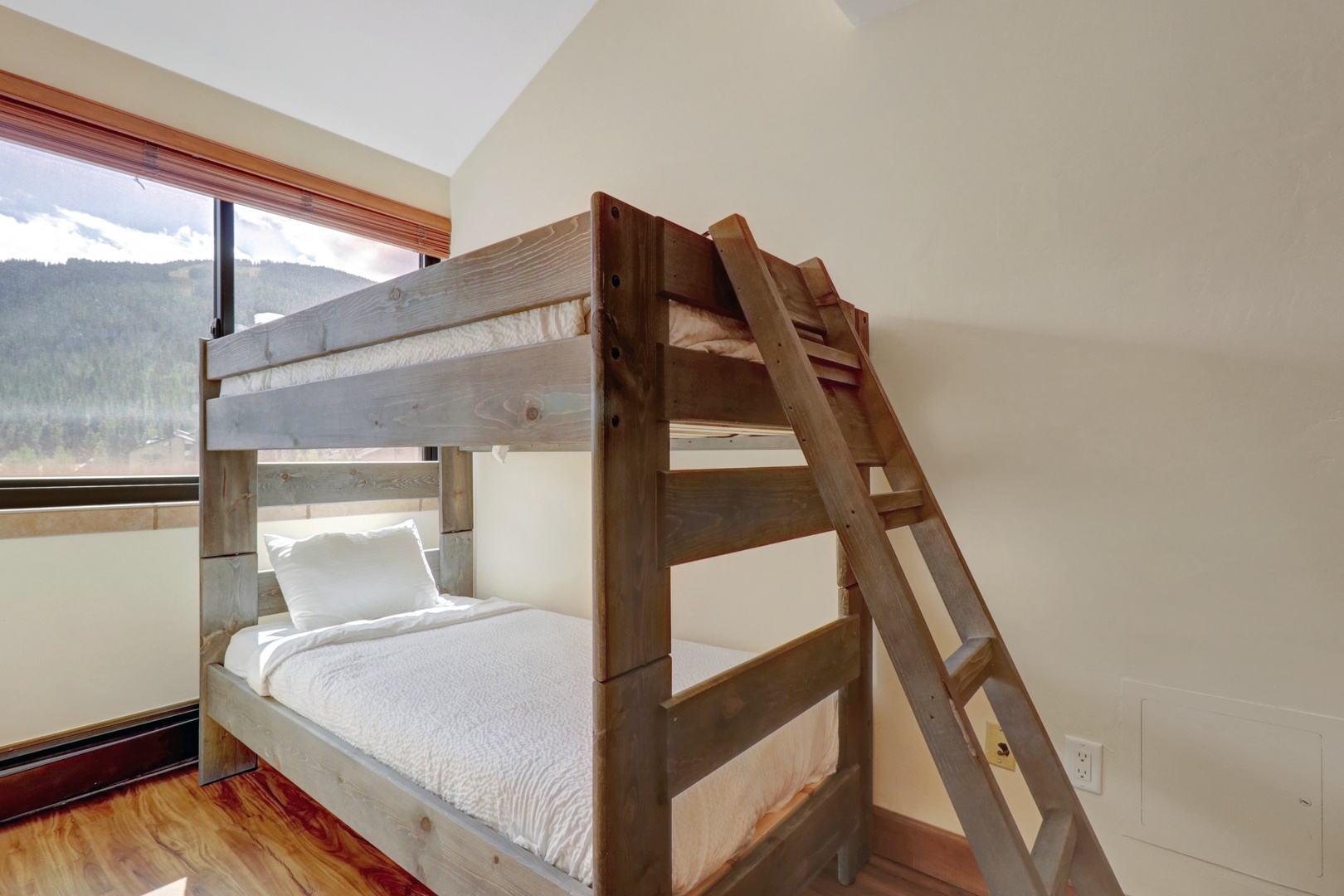 Cozy sleeping nook featuring a sturdy wooden bunk bed and large window showcasing scenic mountain views. Perfect for kids or additional guests.