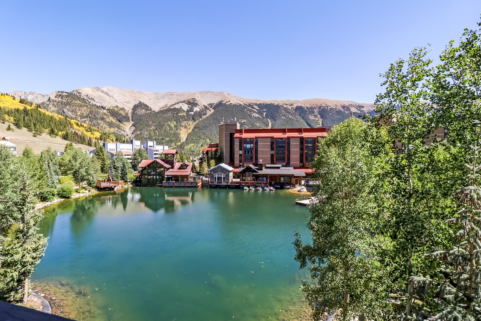 A picturesque alpine retreat nestled beside a tranquil emerald lake, framed by towering mountain peaks and lush summer foliage.