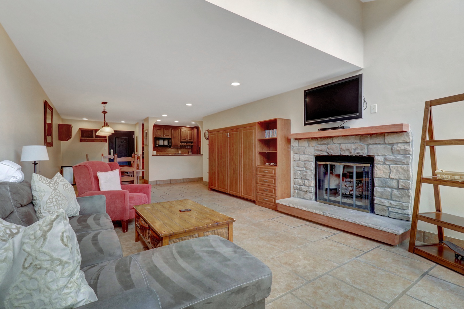 Inviting living space featuring a rustic stone fireplace and wall-mounted TV, with a convenient Murphy bed for additional guests. Open layout flows seamlessly into the dining and kitchen areas.