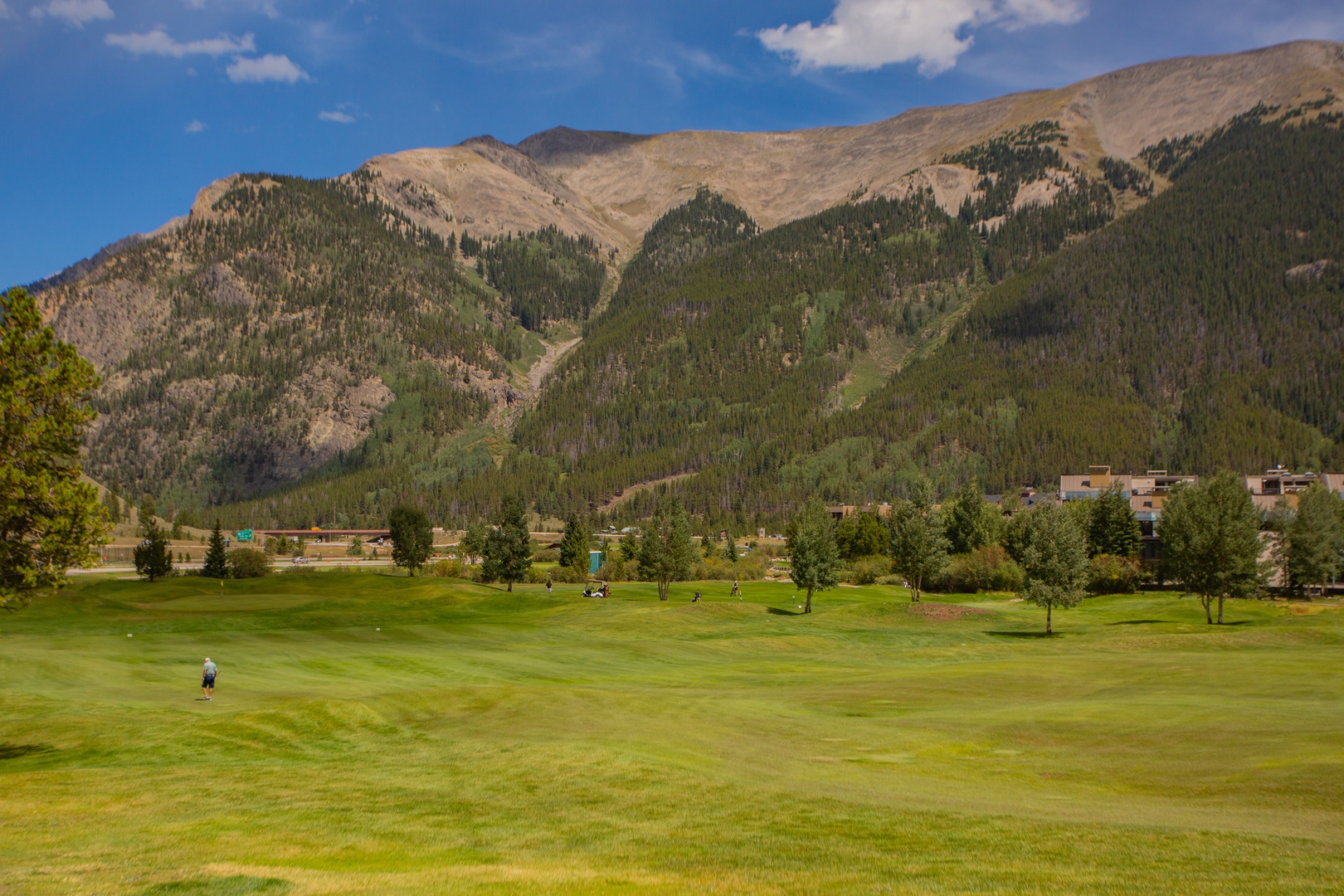 A championship golf course set against dramatic mountain peaks, with lush fairways and scenic alpine terrain surrounding the property.