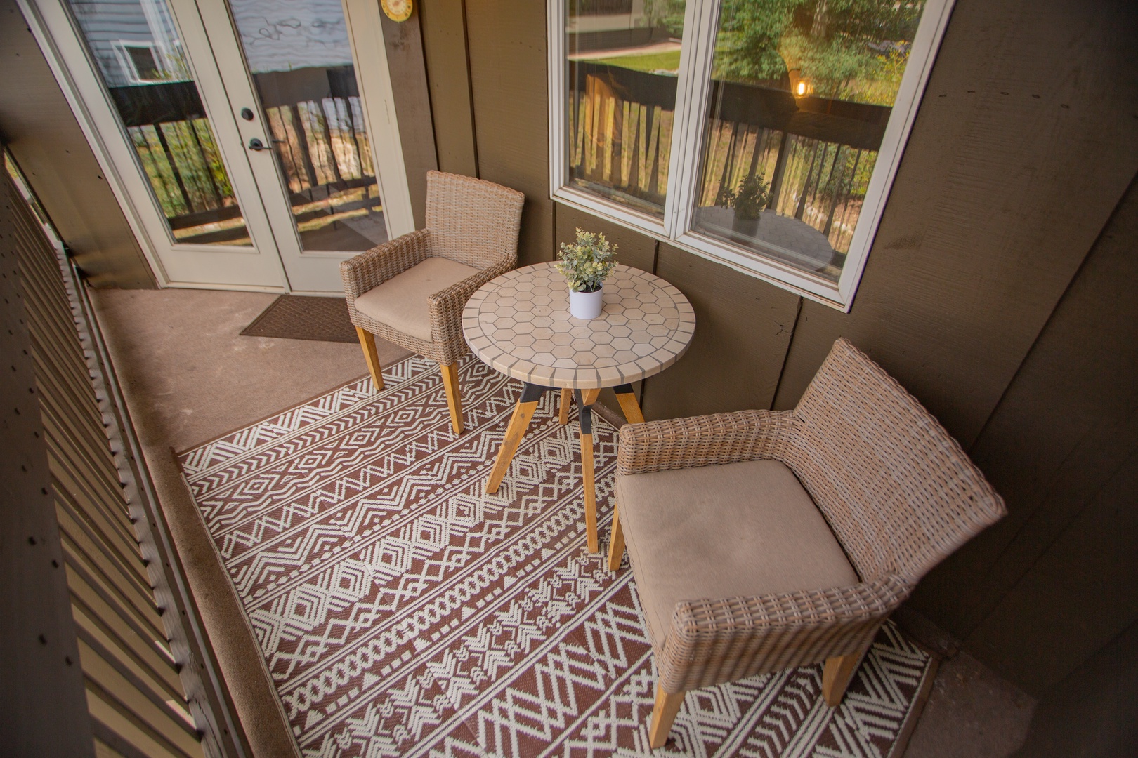 Your private screened porch overlooks peaceful wooded surroundings, with cozy wicker seating and a mosaic-top table perfect for morning coffee or evening relaxation.