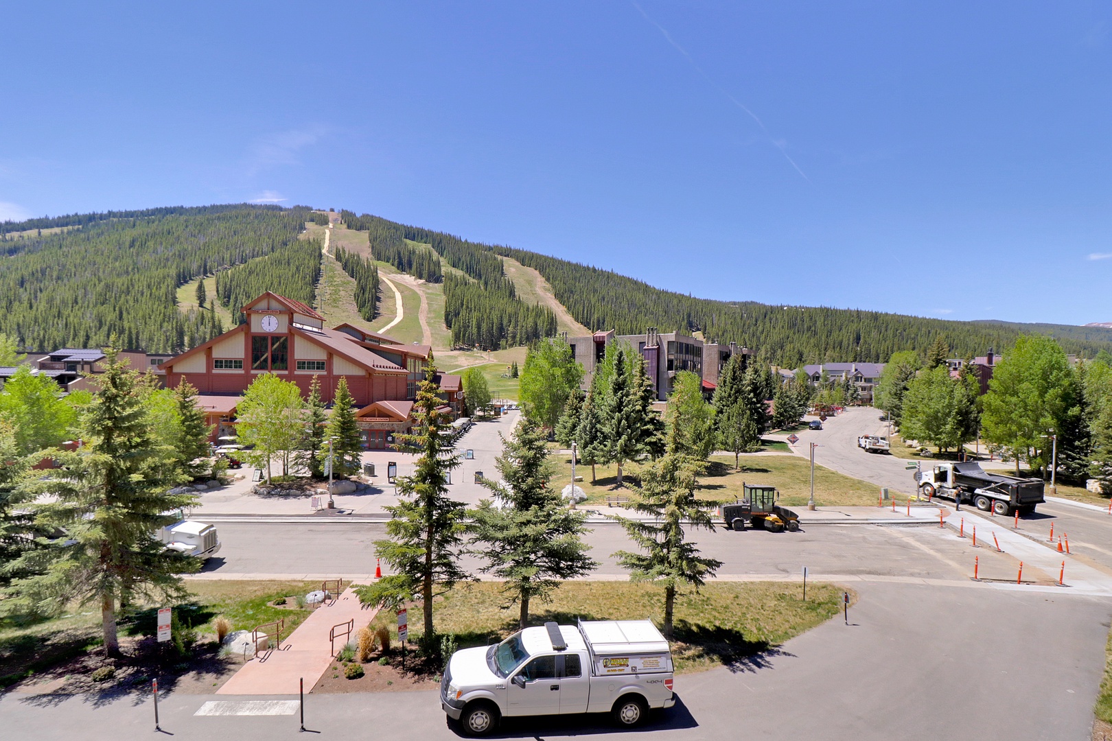 A mountain resort village nestled at the base of ski slopes, surrounded by evergreen forests and accessed by winding mountain roads.