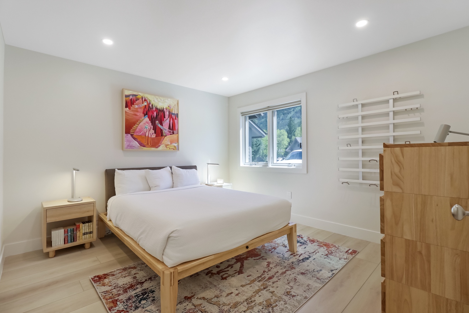 Your serene bedroom retreat features a plush queen bed with crisp linens, warm wood furnishings, and soft natural light streaming through the window—perfect for peaceful mornings and restful nights.