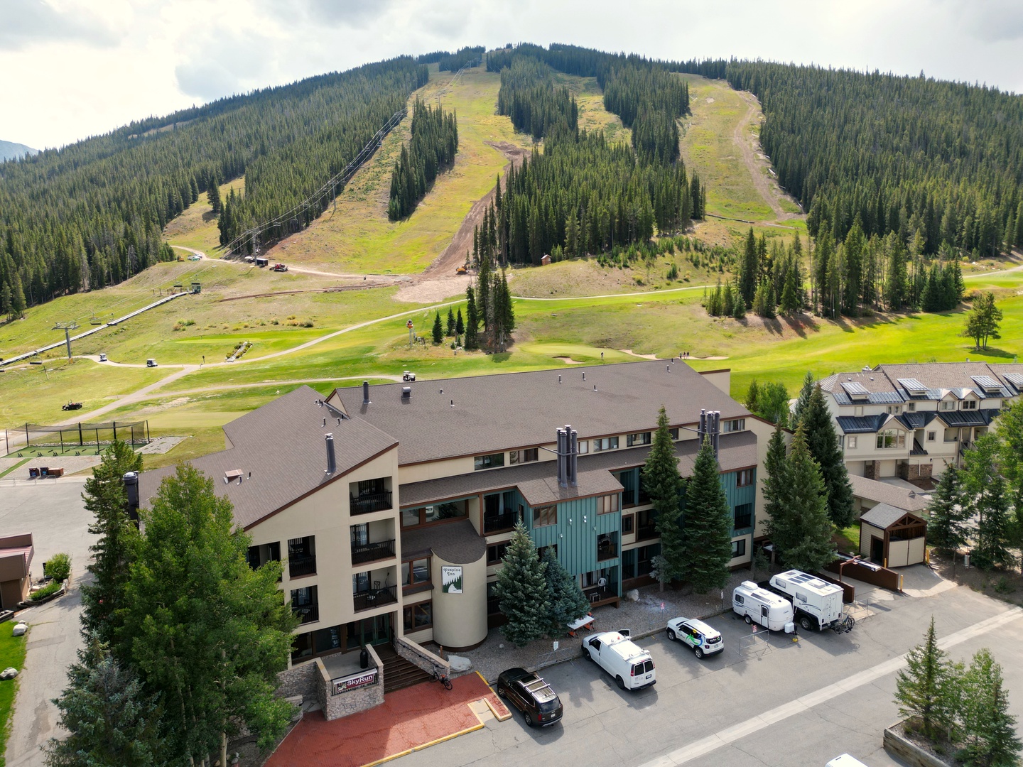 Multi-story mountain resort nestled at the base of ski slopes, surrounded by evergreen forest and summer hiking trails.