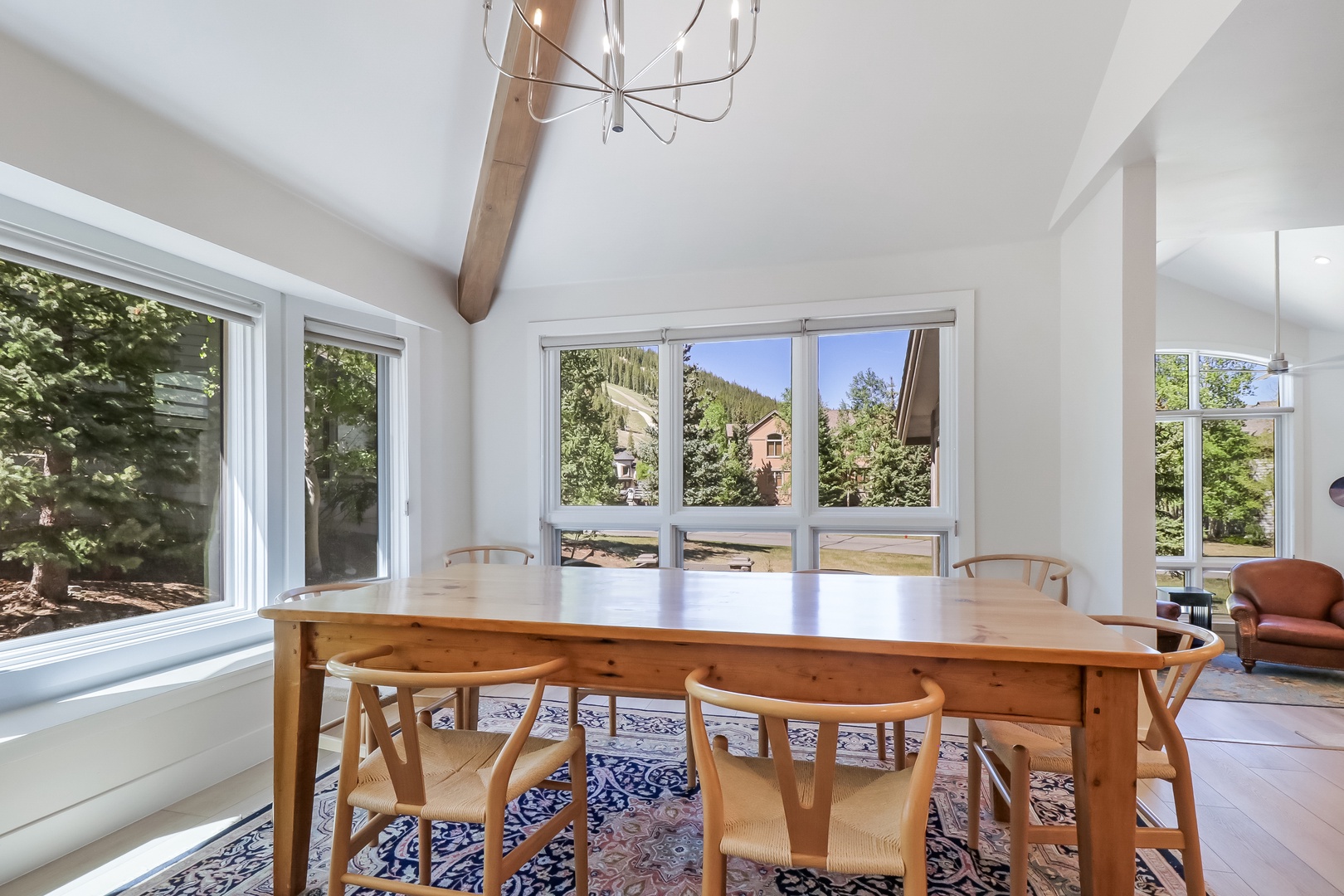 Enjoy meals together at this warm wooden dining table, bathed in natural light. Large windows frame your mountain retreat and the surrounding trees.