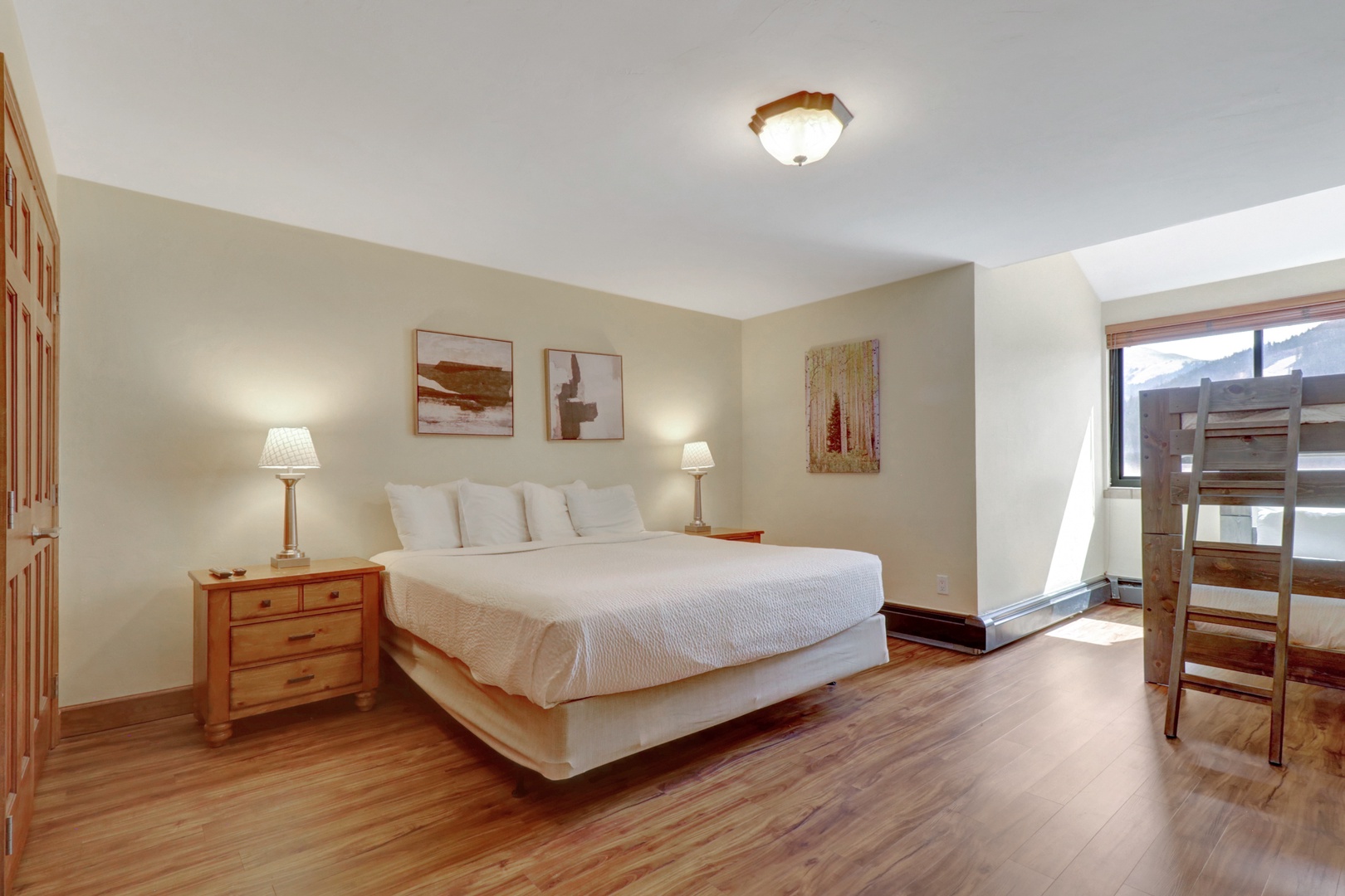 Large king bedroom featuring warm hardwood floors, stylish artwork, and abundant natural light. A peaceful retreat after a day of mountain adventures.