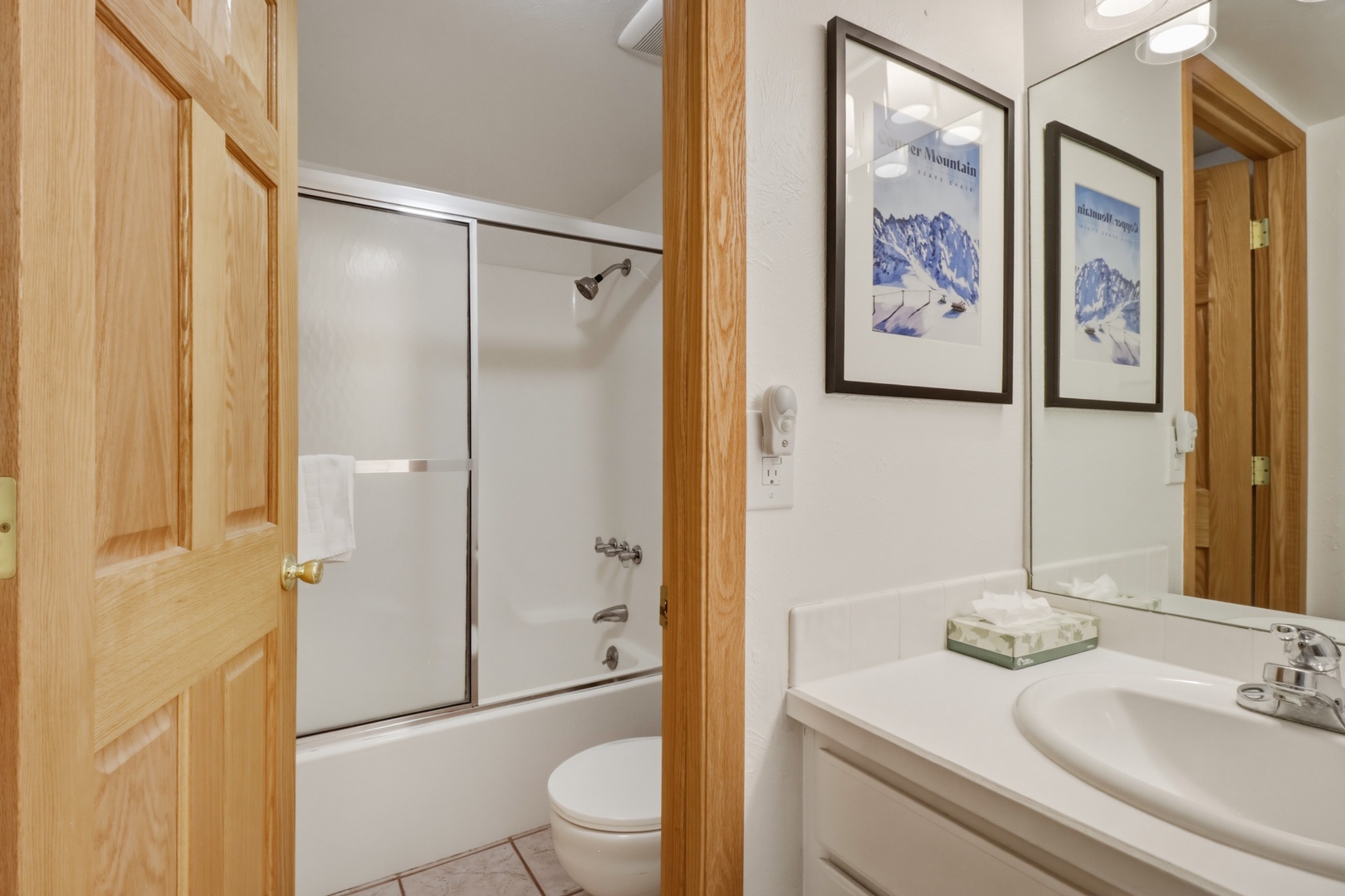 Your private bathroom features a relaxing tub-shower combo, clean white surfaces, and thoughtful mountain artwork.