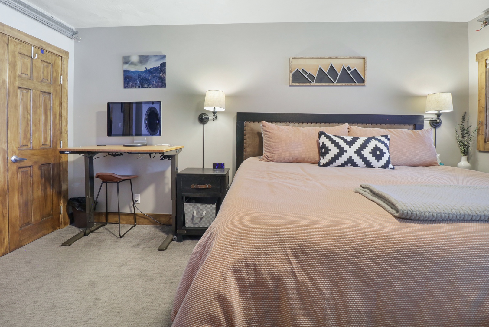 Settle into your cozy mountain retreat bedroom where soft pink linens invite restful sleep, while the rustic desk by the window creates your perfect workspace with inspiring artwork above.
