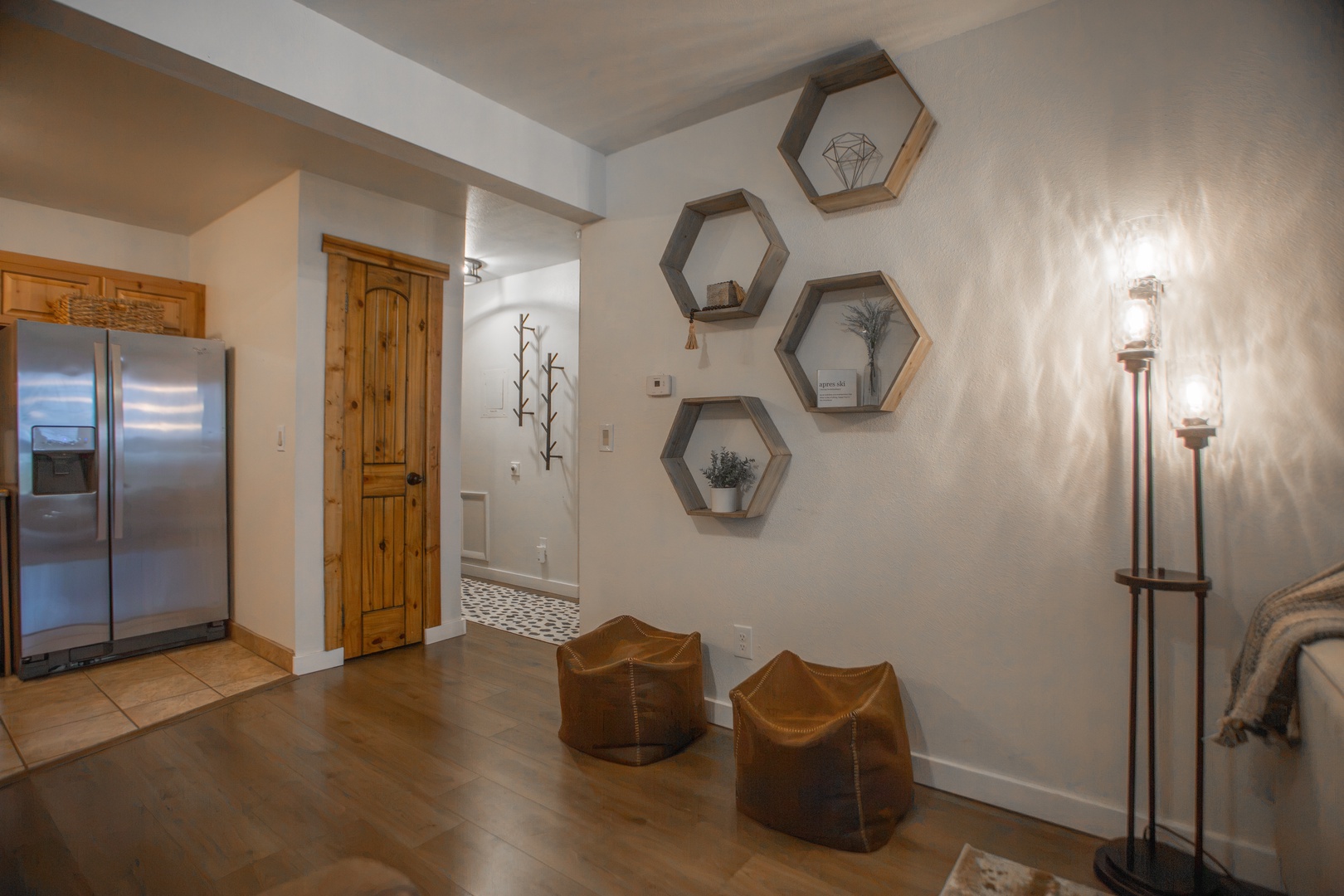 A thoughtfully designed living space welcomes you with warm wood floors, artful hexagonal shelving, and cozy leather seating. The open layout flows seamlessly into modern kitchen amenities, creating an inviting home base for your stay.